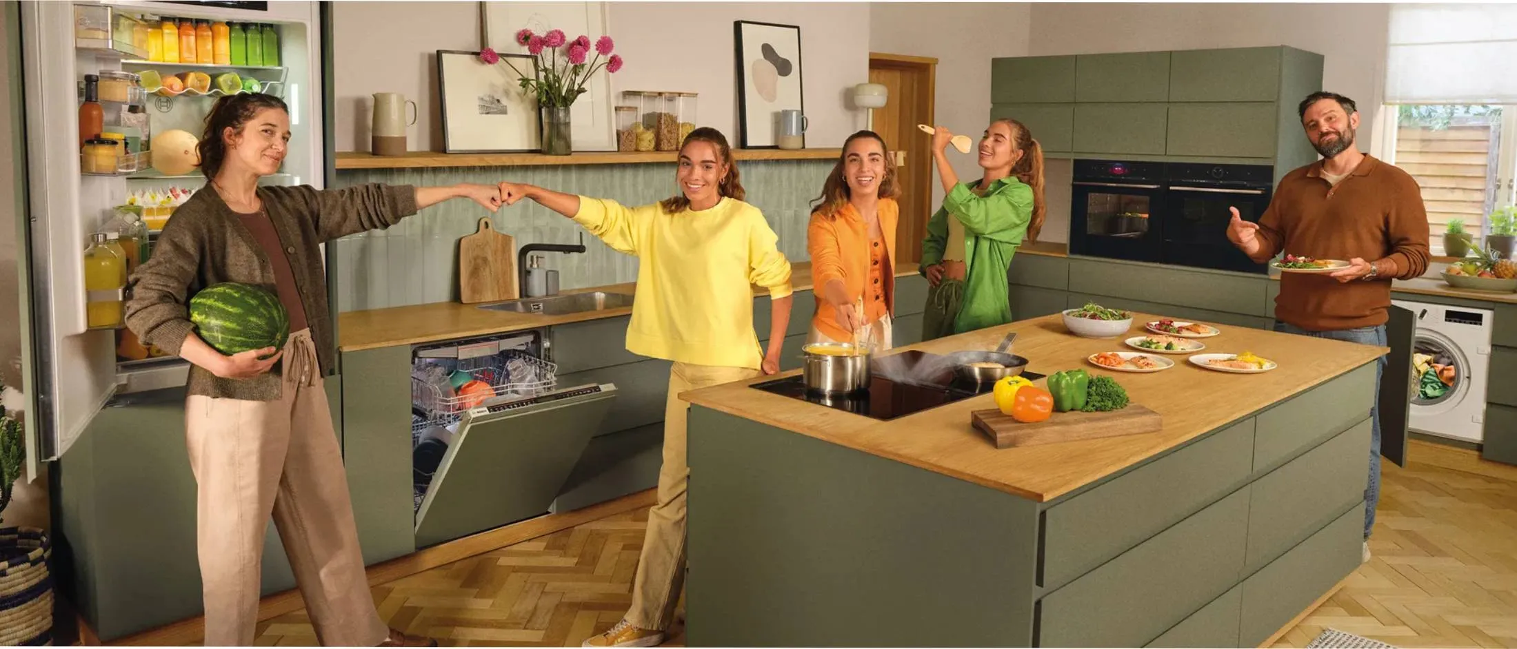 Hombre en el delantal verde de pie en la cocina, señalando a las verduras en la tabla de cortar.
