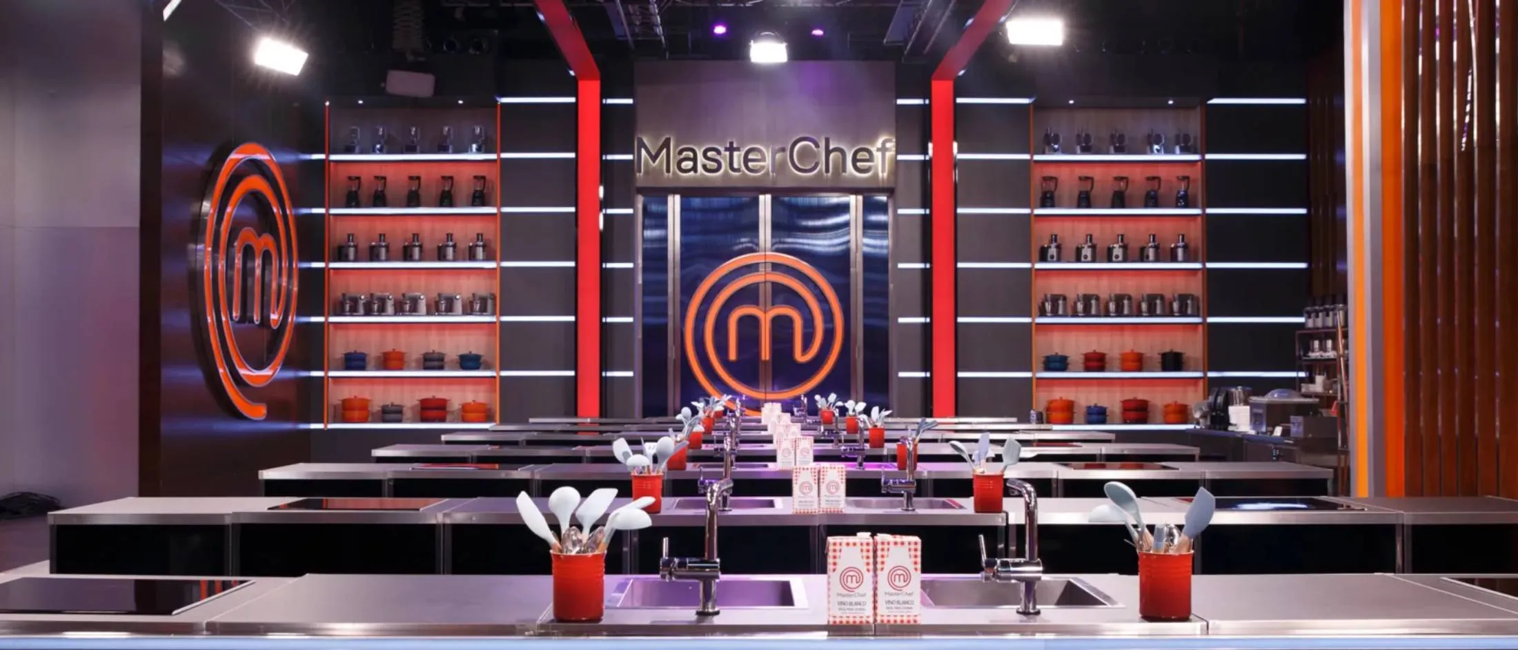 Moderno juego de cocina MasterChef, con letreros de color naranja vibrante, elegantes estaciones de cocina y utensilios e ingredientes bien ordenados.