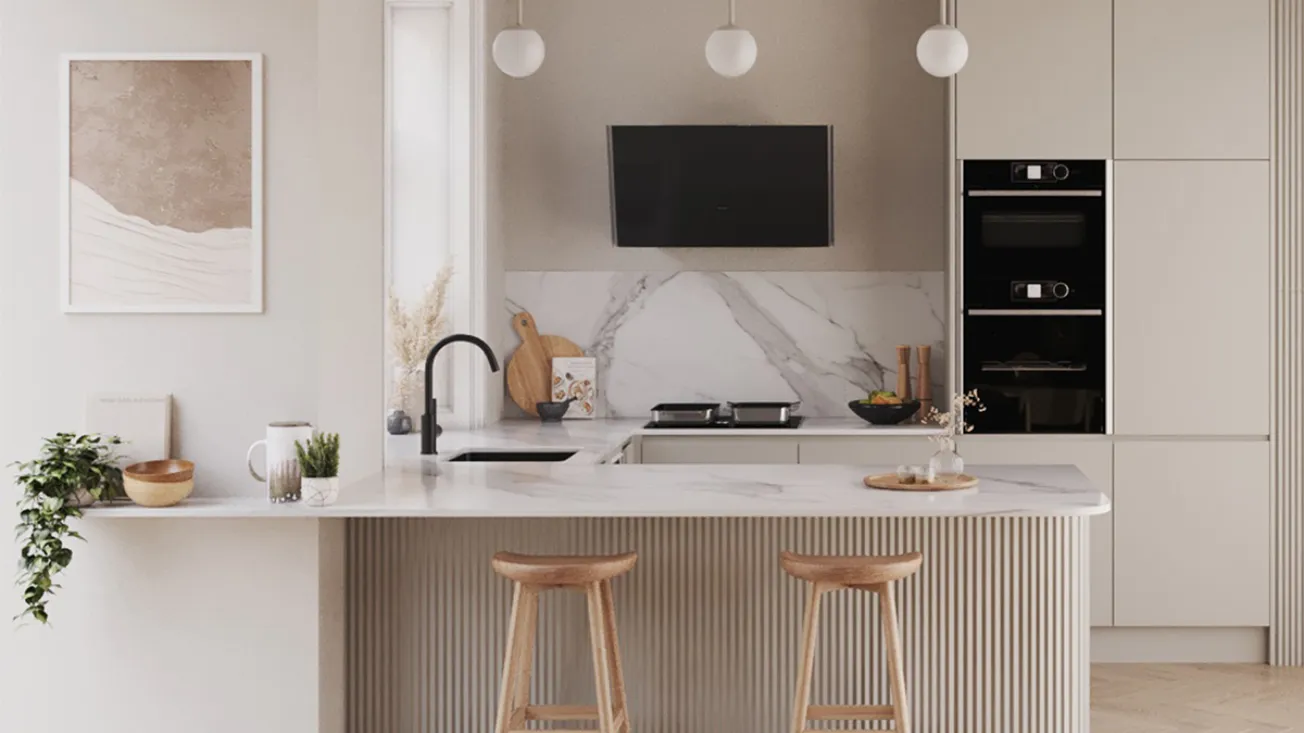 Light, neutral kitchen with a marble countertop and fluted-front island with two wooden bar stools, black sink faucet, wall-mounted black oven hood over a cooktop, stacked black built-in ovens, three globe pendant lights, small plants and framed artwork