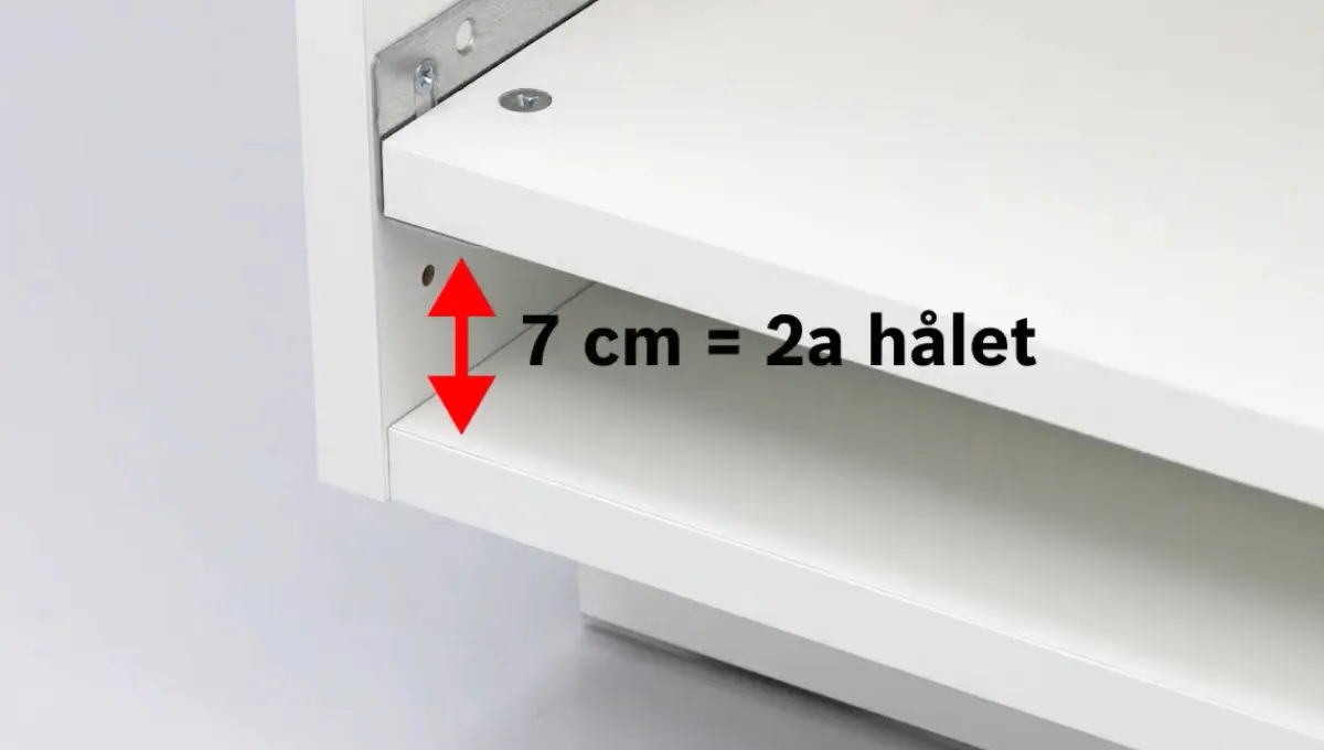 Bilden visar ett vitt skåp med ett varningstecken som anger en 7 cm gap, vilket är lika med ett 2: a hål.