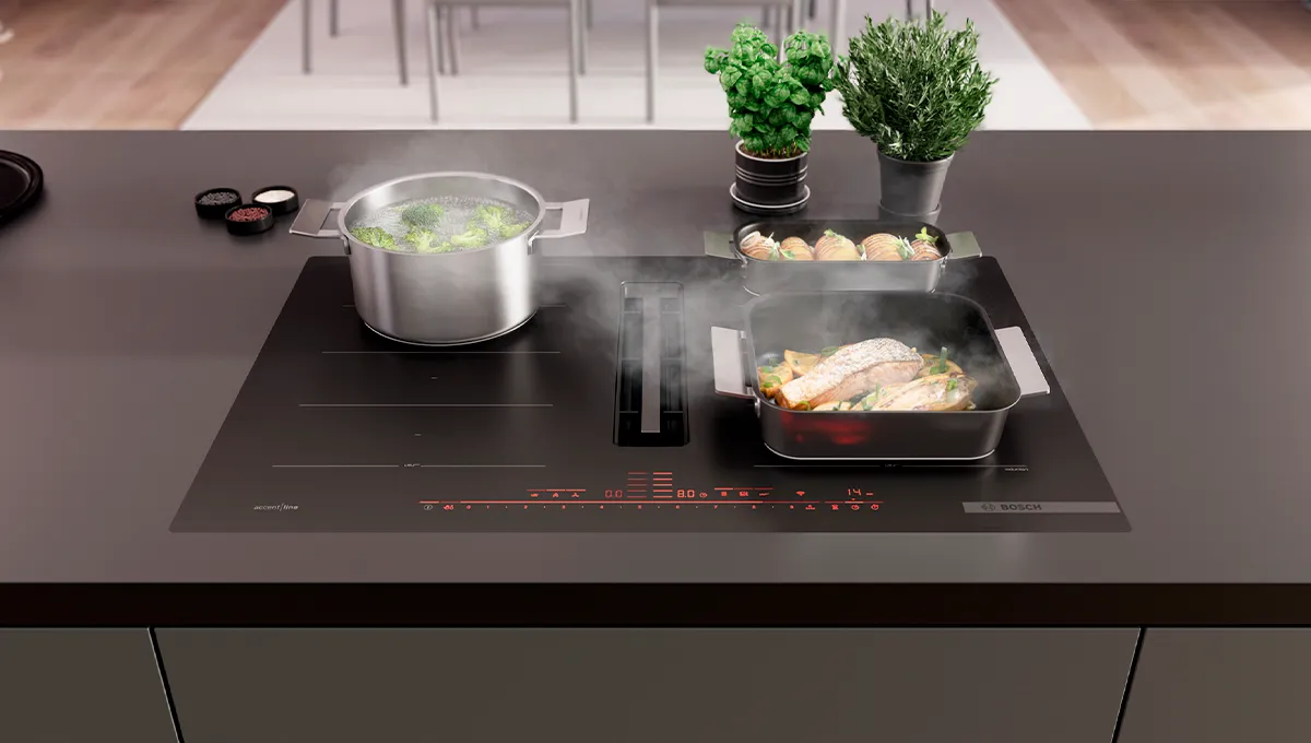 Индукционен плот Bosch с тенджери, в които се готвят зеленчуци и риба, с билки на заден план на плота.