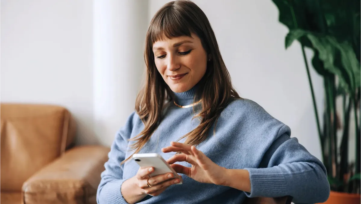 Jeune femme en pull bleu avec smartphone sur le canapé dans le salon.
