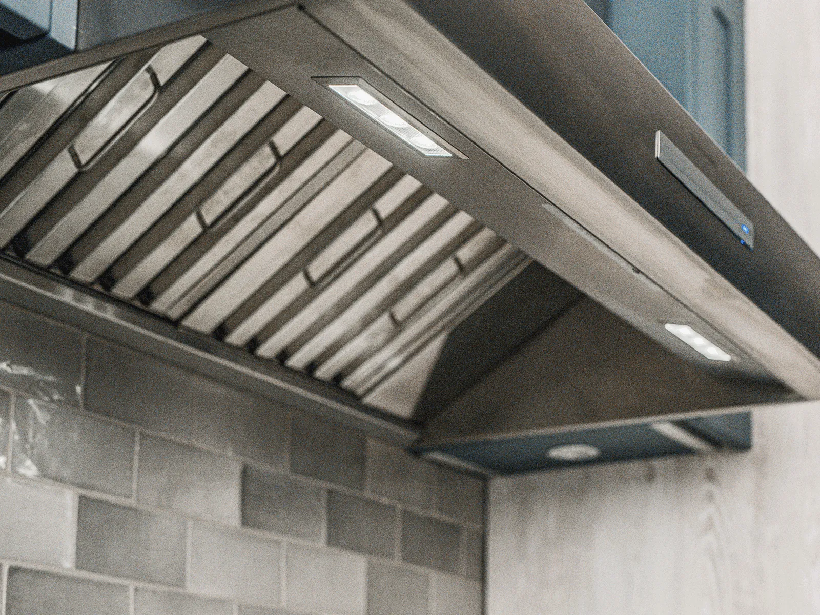 Modern kitchen stovetop with a stainless steel pot, blue cabinets, white textured tile backsplash, and a wall-mounted pot filler faucet.