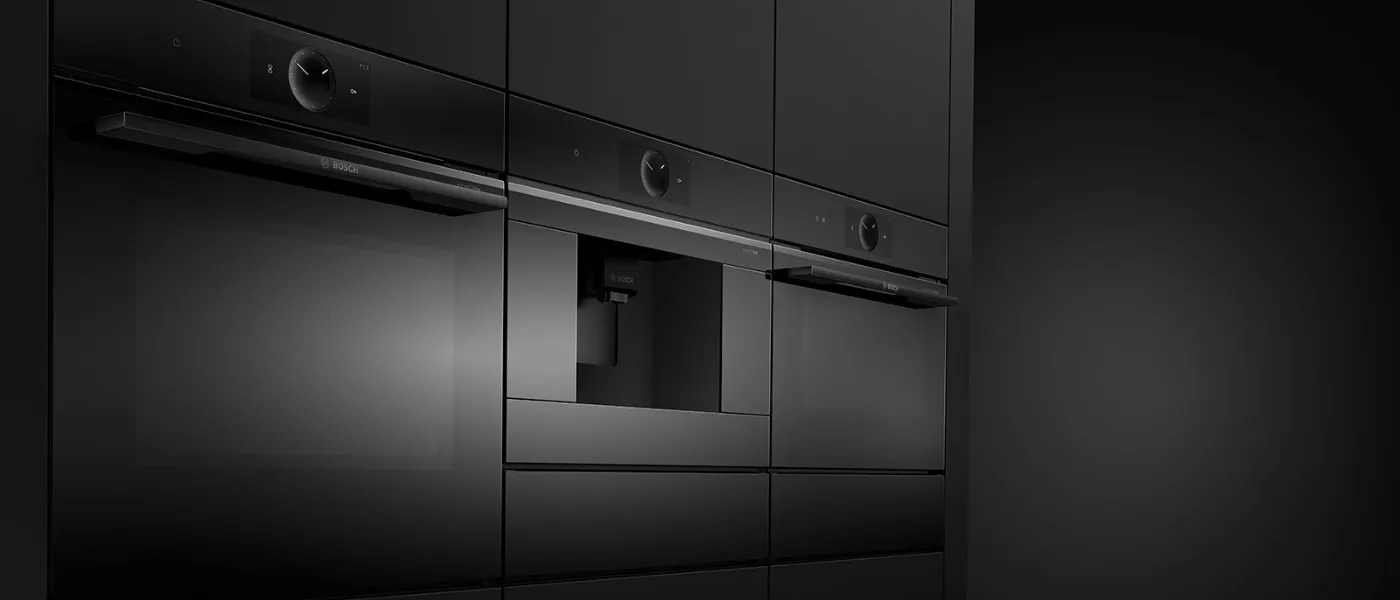 Trei cuptoare încorporate Bosch negre, cu aparat de cafea integrat, în mobilier de bucătărie modern.
