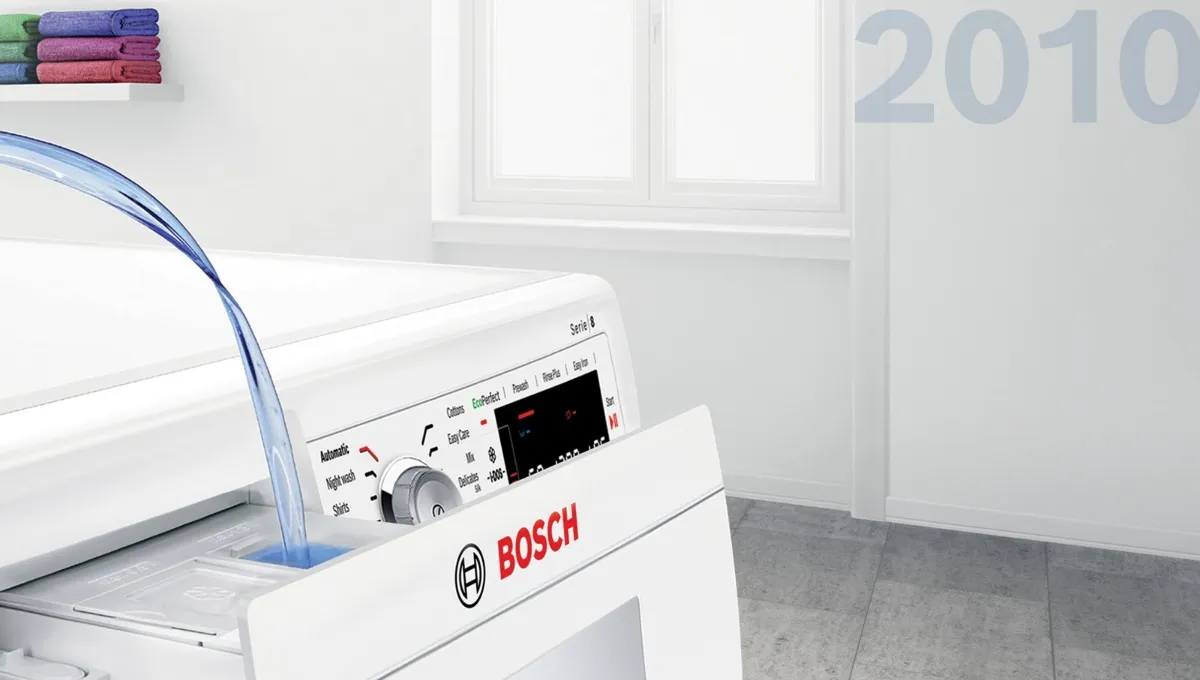 Bosch washing machine with liquid flowing into the detergent drawer, coloured towels on shelf, 2010.