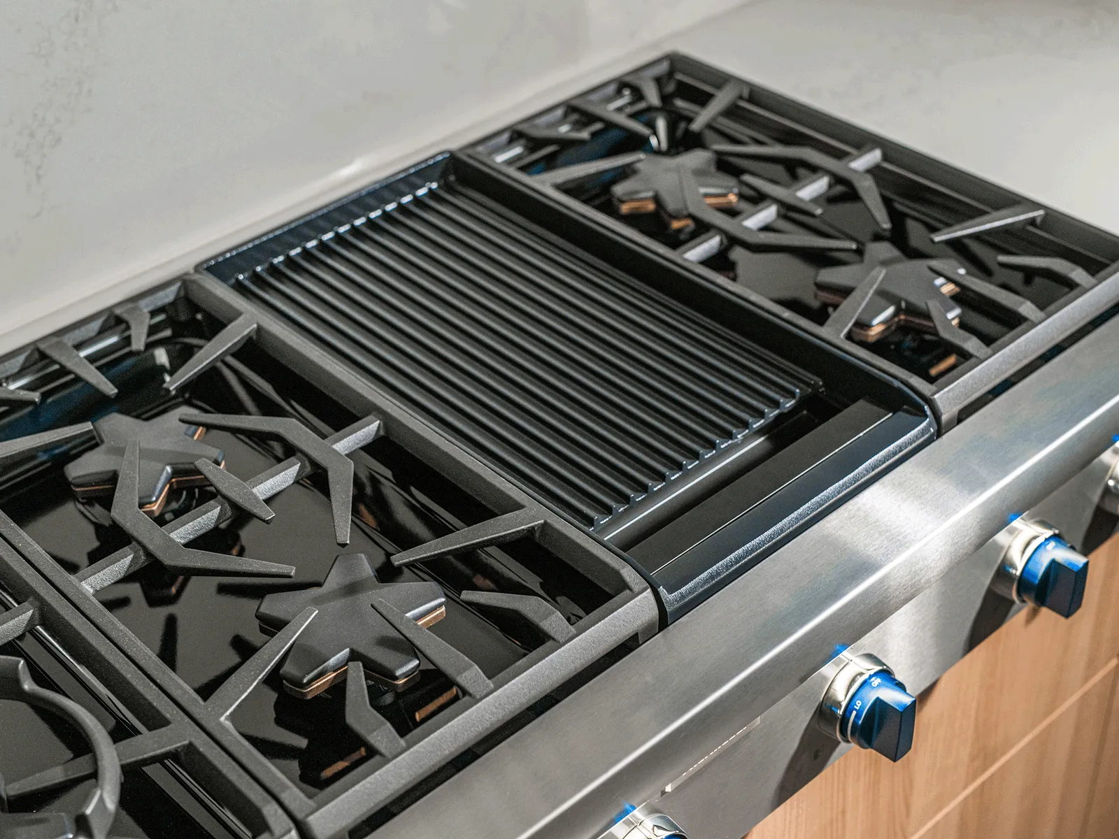 Two hands lifting a ridged cast-iron griddle from the top of a stainless-steel gas range with a tiled backsplash.