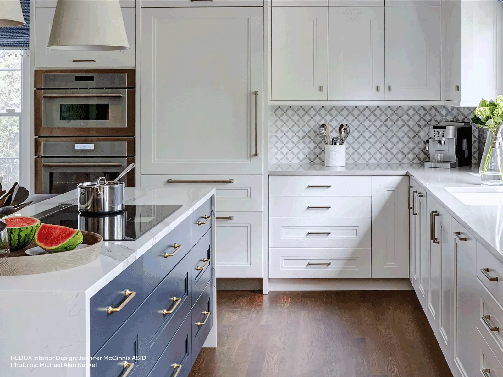 Modern kitchen with white cabinets, blue island, stainless steel appliances, wooden floor, and a countertop featuring a watermelon and cooking pot.