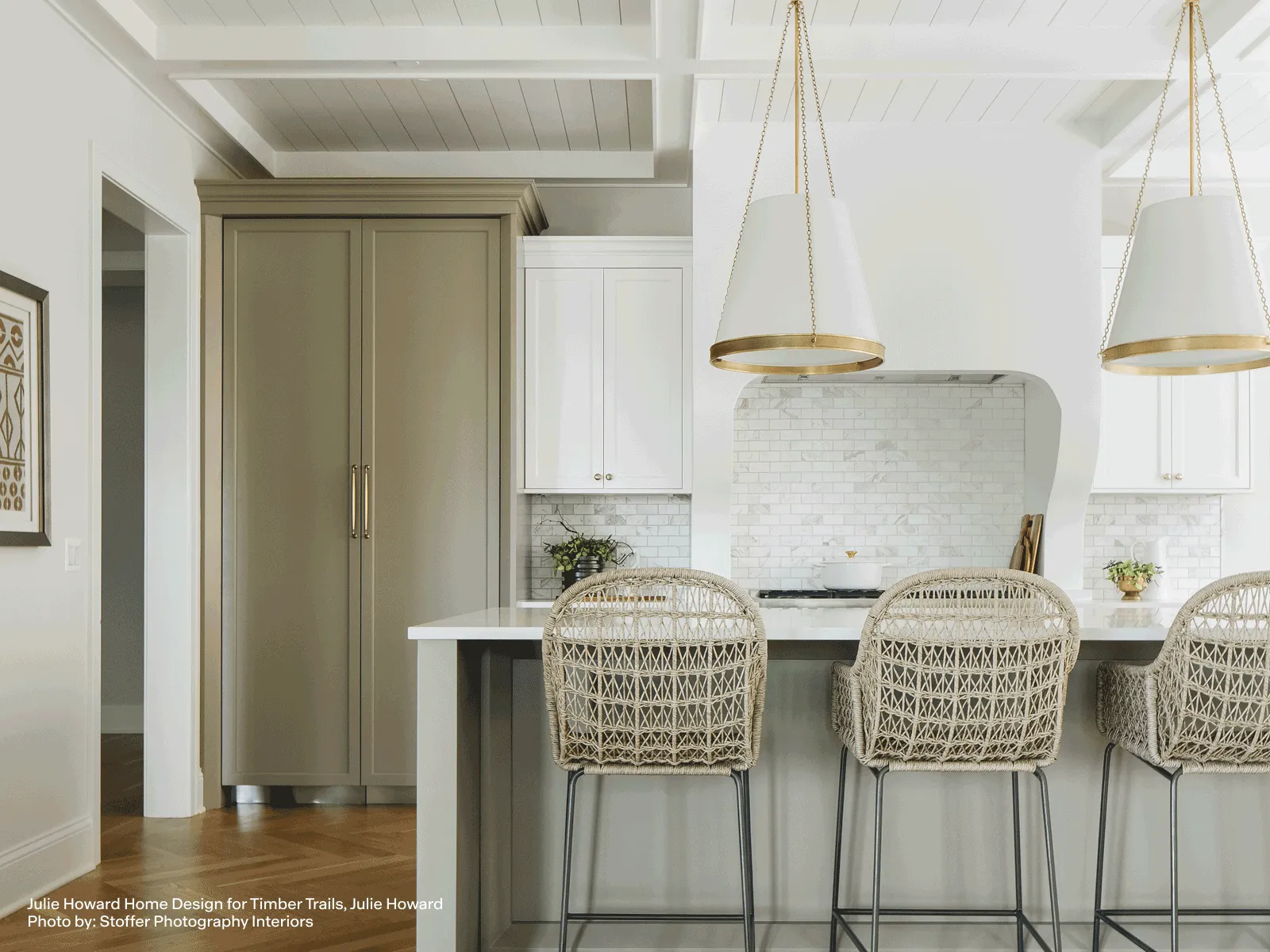 Bright modern kitchen with white cabinets, wicker bar stools, metal appliances, and pendant lights over a large island.
