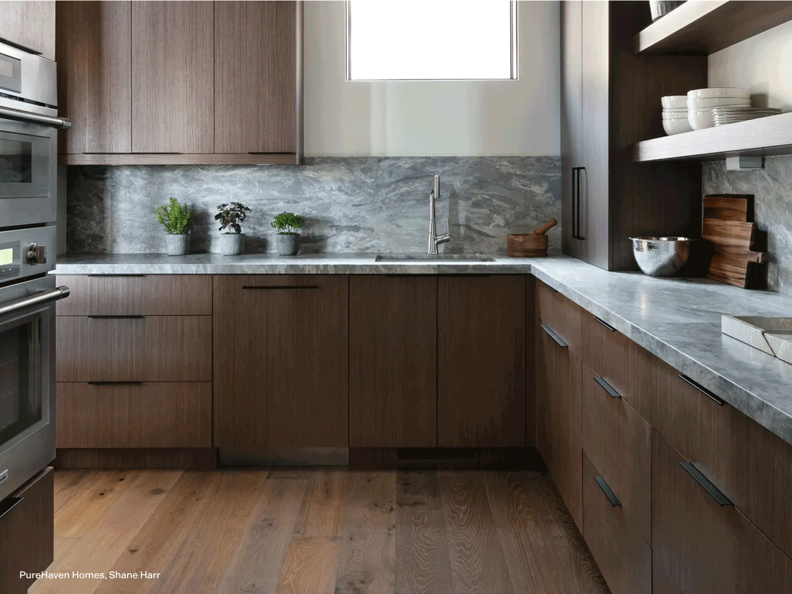 A modern kitchen featuring a custom-paneled Thermador dishwasher that matches the dark wood cabinets, complemented by grey marble countertops.