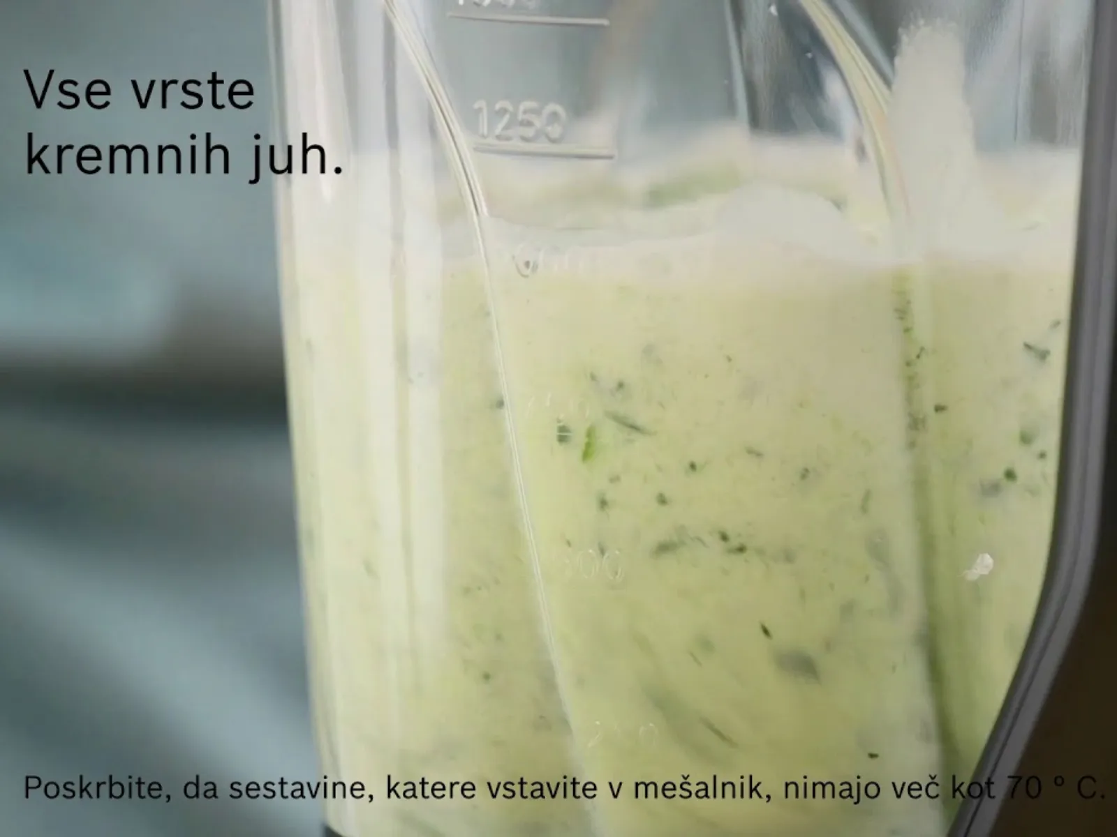 Približek posode mešalnika, v katero se vliva kremasta juha, v njej pa so vidna zelišča