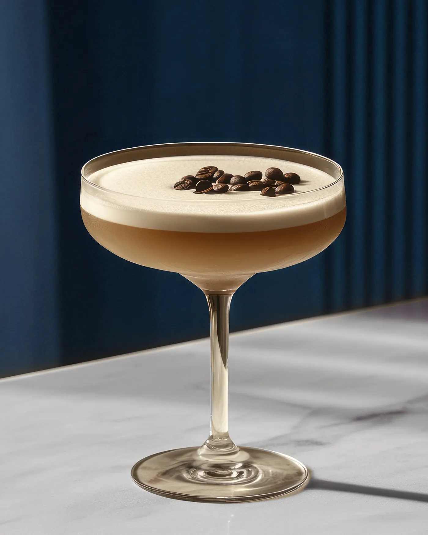 Cocktail glass with layered espresso martini topped with coffee beans on a white surface next to a small metallic container