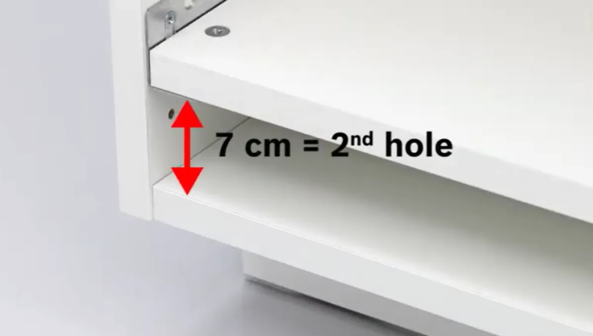Kuva esittää valkoisen kaapin, jossa varoitusmerkki osoittaa 7 cm:n raon, mikä vastaa toista reikää.