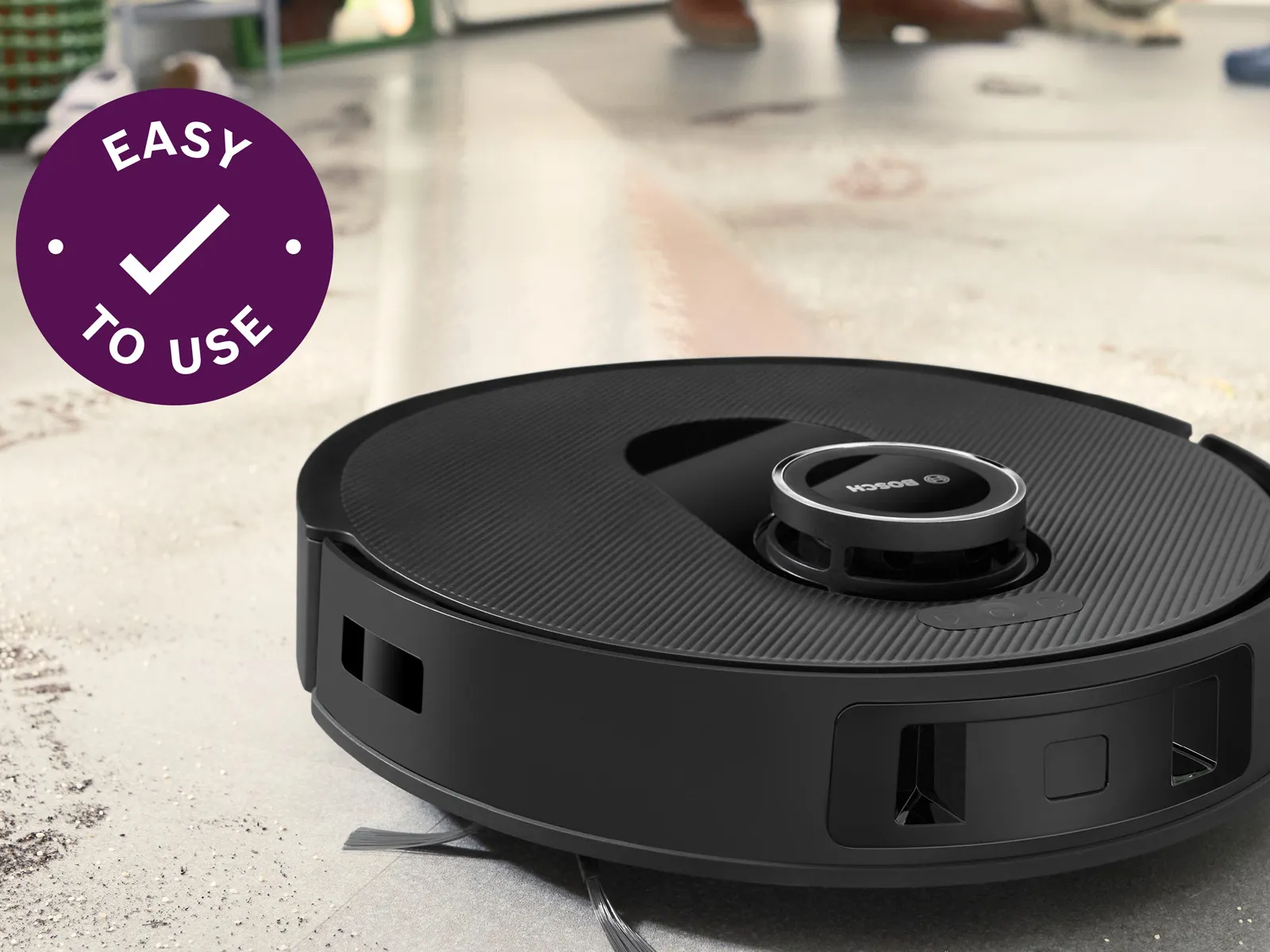 A close-up of a Bosch robot vacuum on a dirty floor, with an "Easy to Use" icon and text that says, "One-tap scheduling gives you freedom."