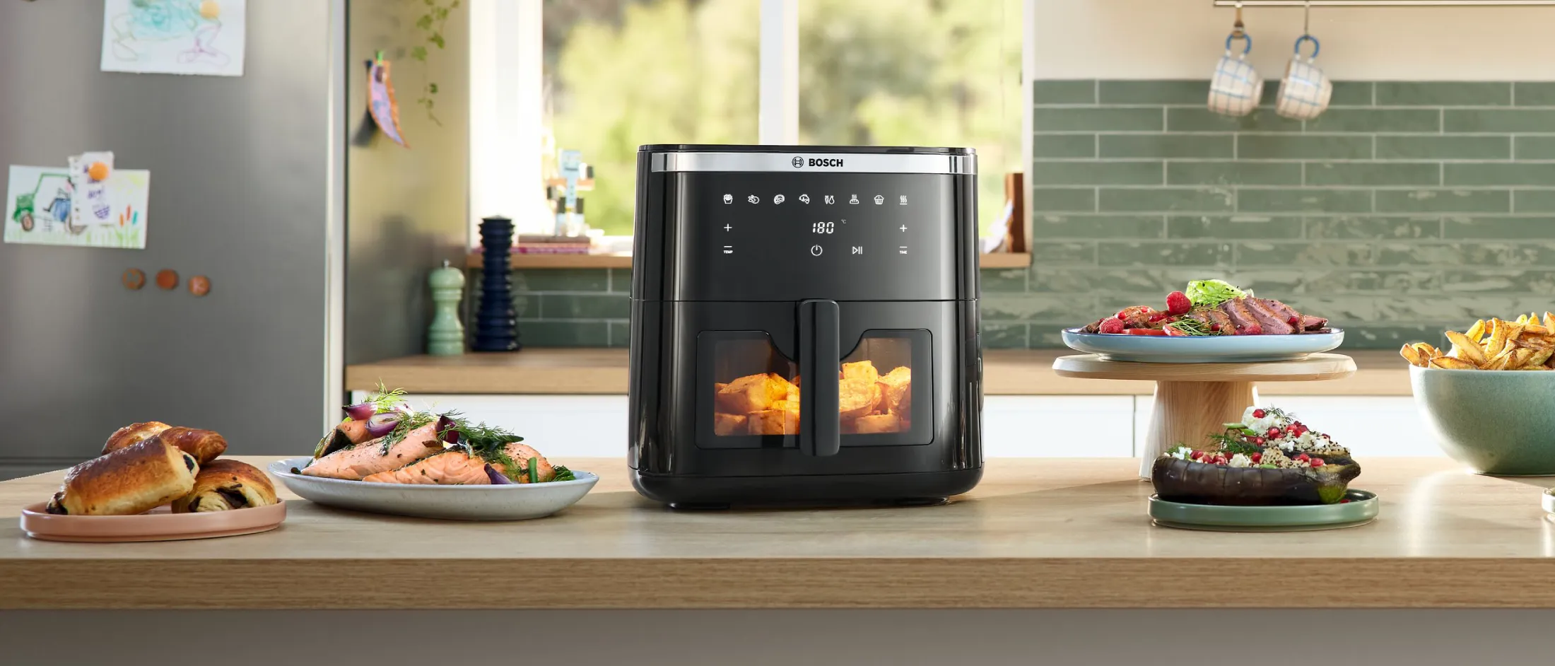 Three Bosch Air Fryers standing on a kitchen counter with various dishes next to it.