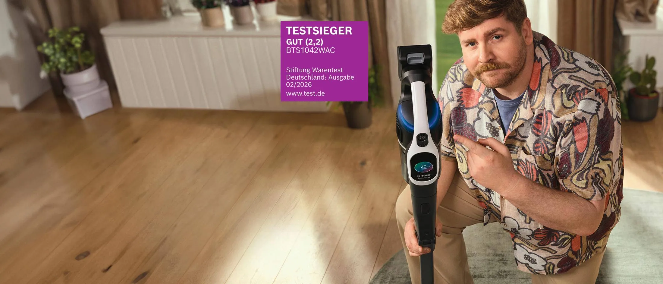 Ein blonder Mann mit Bart und buntem Hemd präsentiert den Akku-Staubsauger Testsieger Unlimited 10 von Bosch.