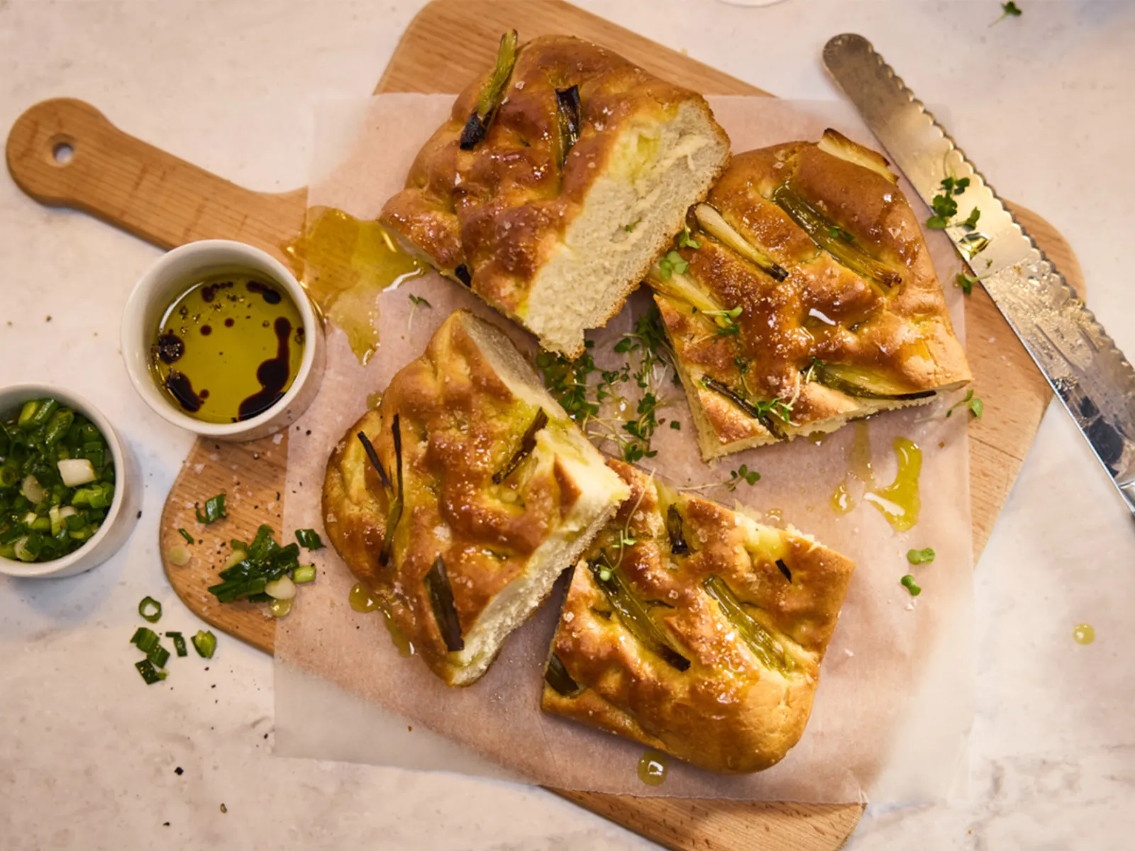 Freshly baked focaccia topped with green onions, drizzled with olive oil, served on a wooden cutting board with dipping sauces.