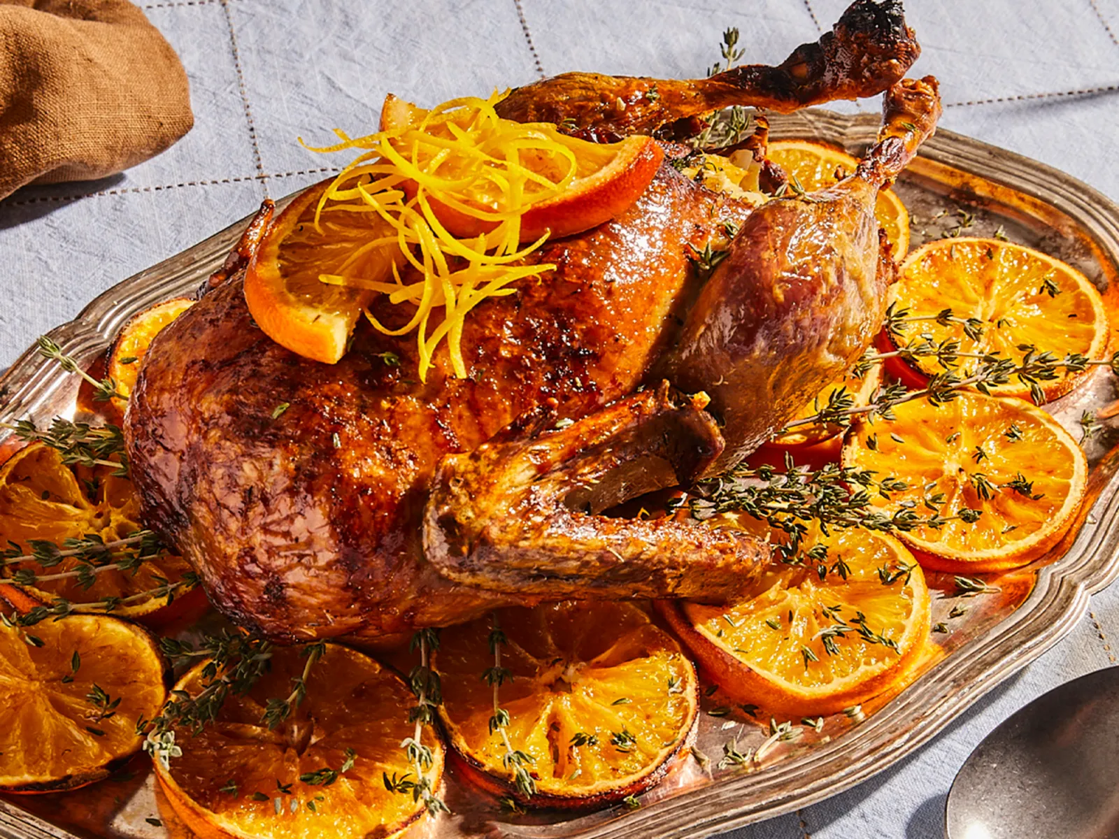 Roasted duck garnished with orange slices, served on a platter with a pie and other holiday decorations.