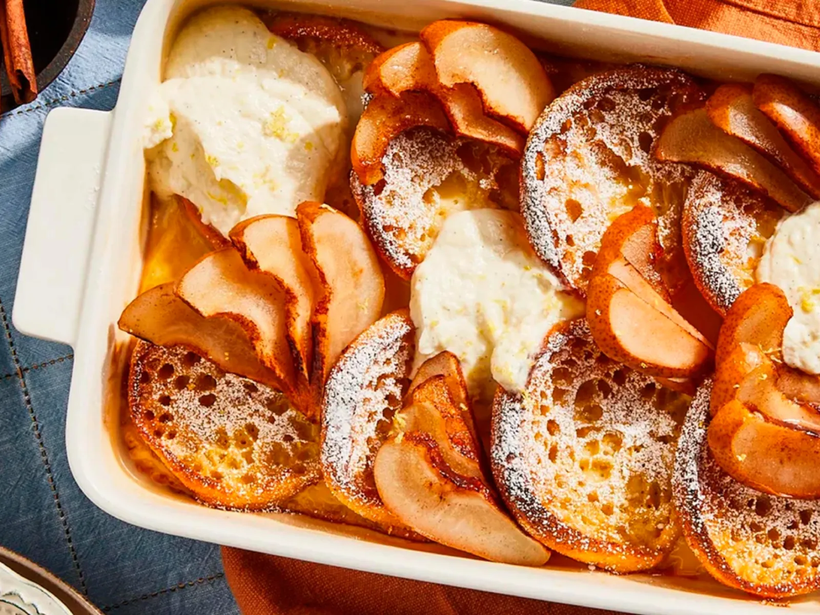 Baked apple slices with cinnamon and sugar in a white baking dish, surrounded by orange napkins and utensils.