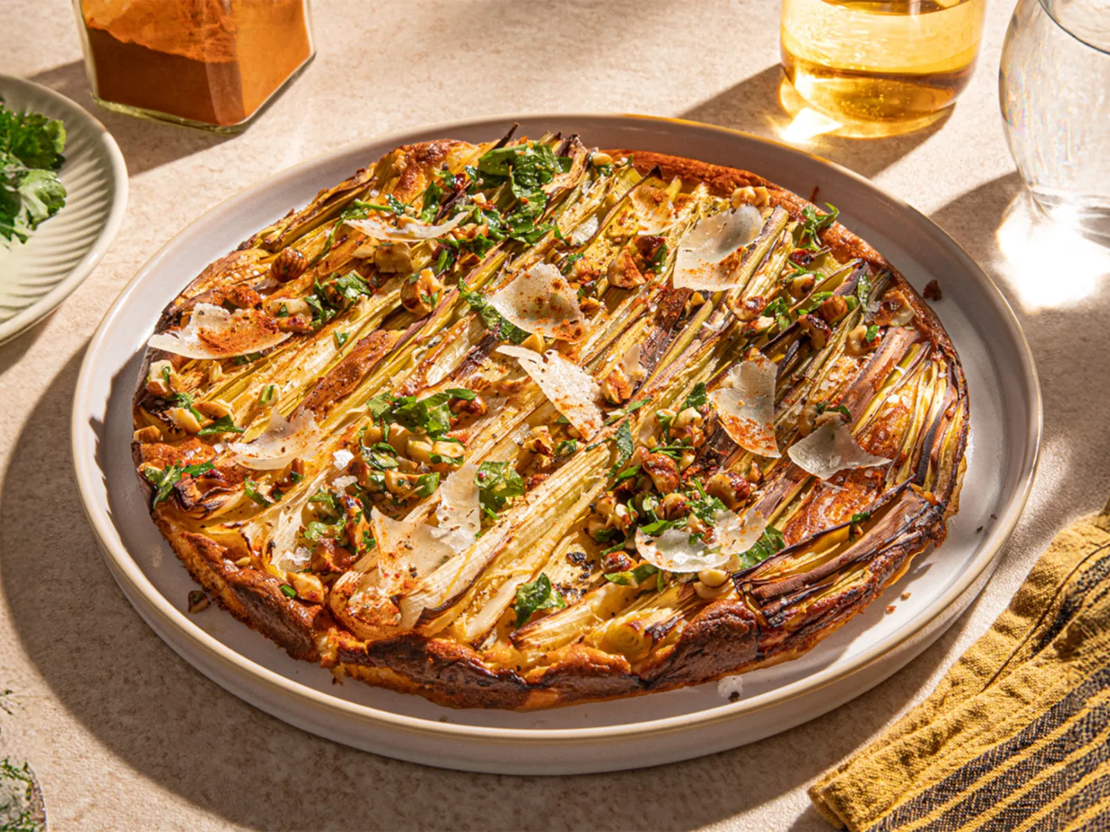 A beautifully arranged savory tart topped with green onions, herbs, and cheese, surrounded by fresh cilantro and a glass of water.