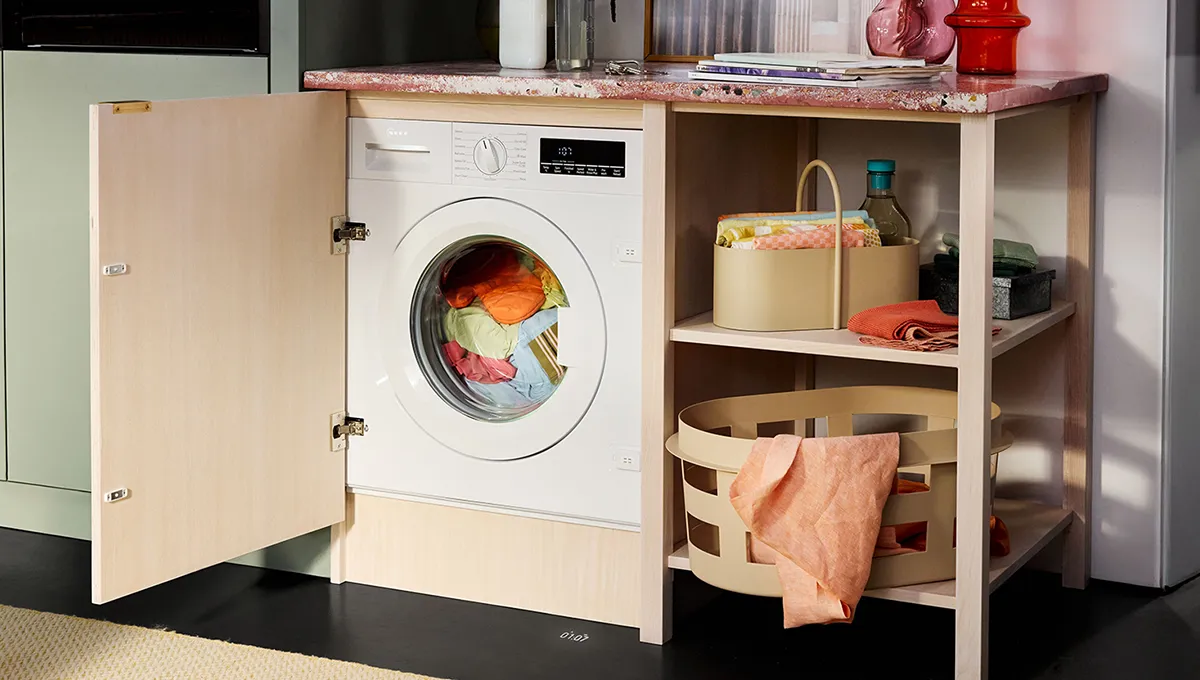 A laundry area featuring a washing machine behind an open wood cabinet door, colorful laundry inside, and organized storage below.