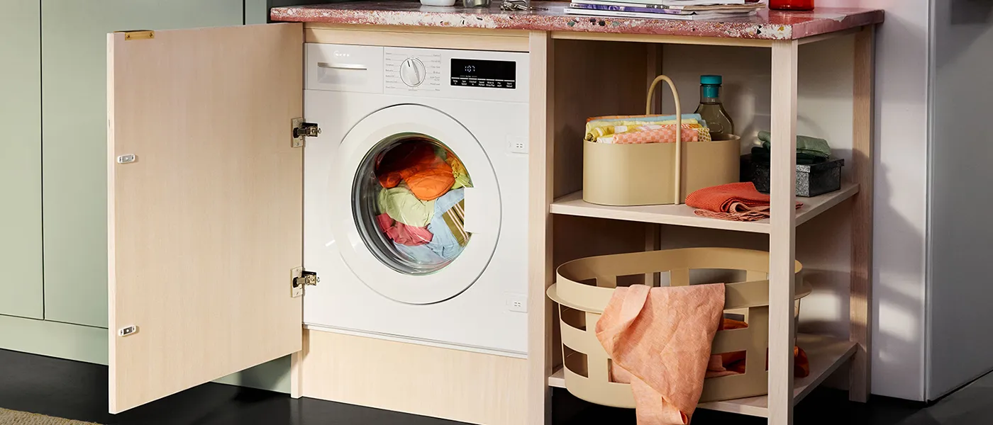 A laundry area featuring a washing machine behind an open wood cabinet door, colorful laundry inside, and organized storage below.