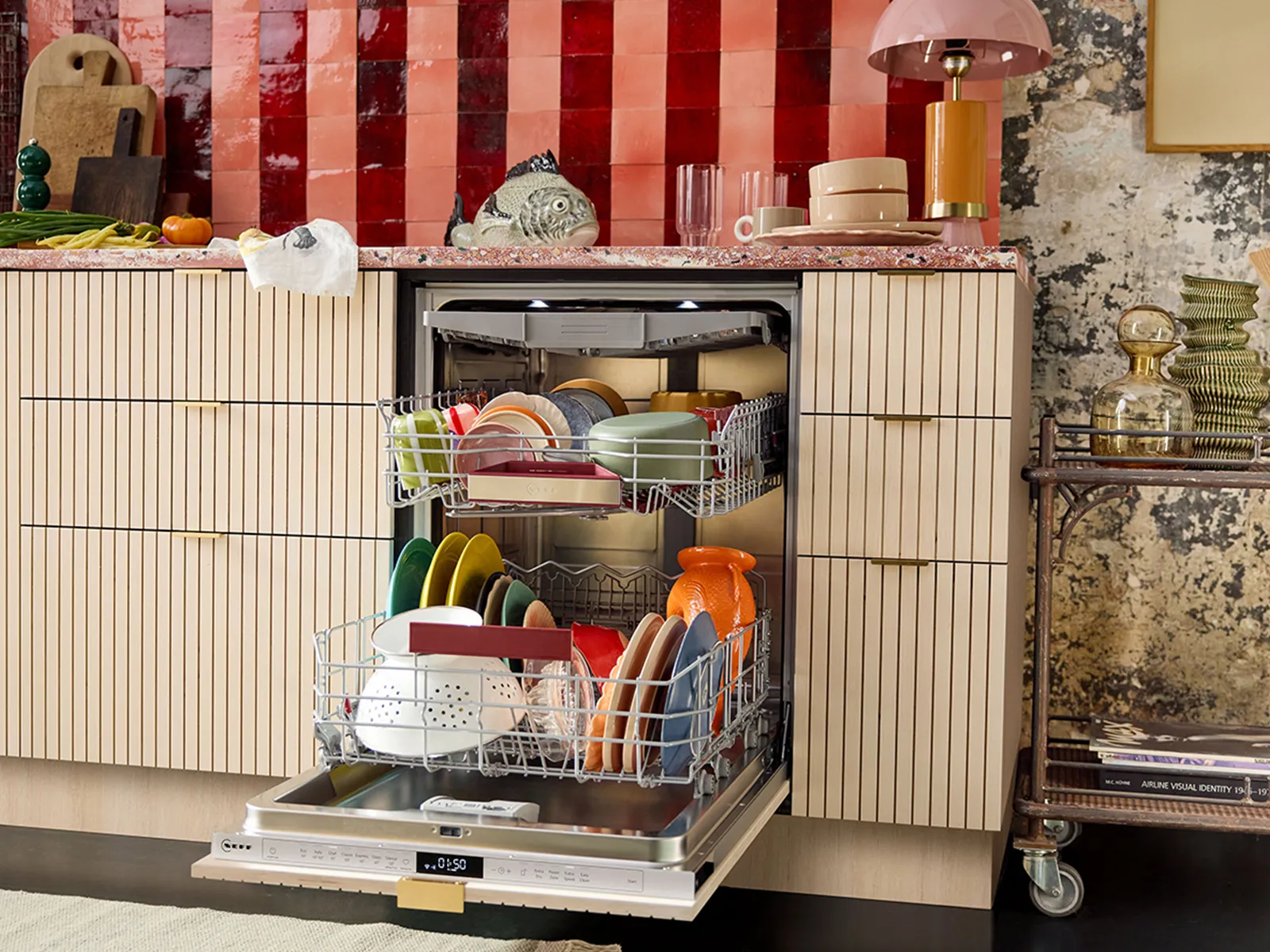 A stylish kitchen featuring a partially open dishwasher filled with colorful dishes, set against a vibrant red tile backsplash.