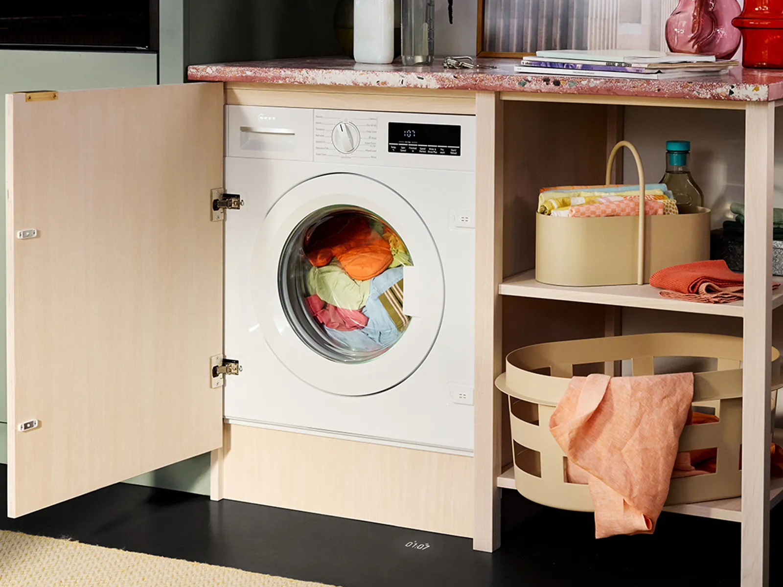 Перална машина с цветни дрехи, дървени рафтове и организирани кошници.