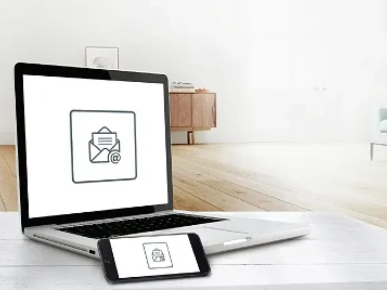 Ordinateur portable et appareil mobile affichant une icône d’enveloppe, avec un intérieur de salon moderne en arrière-plan.