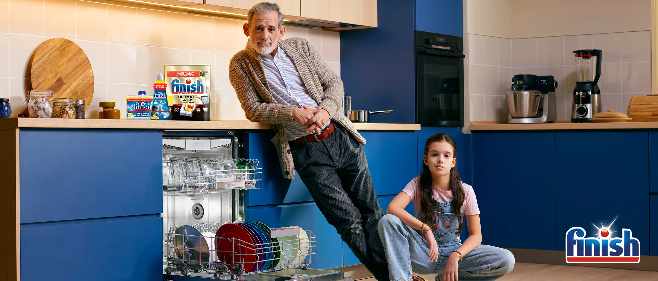Adult and child in kitchen next to open Dishwasher with Finish pack on top