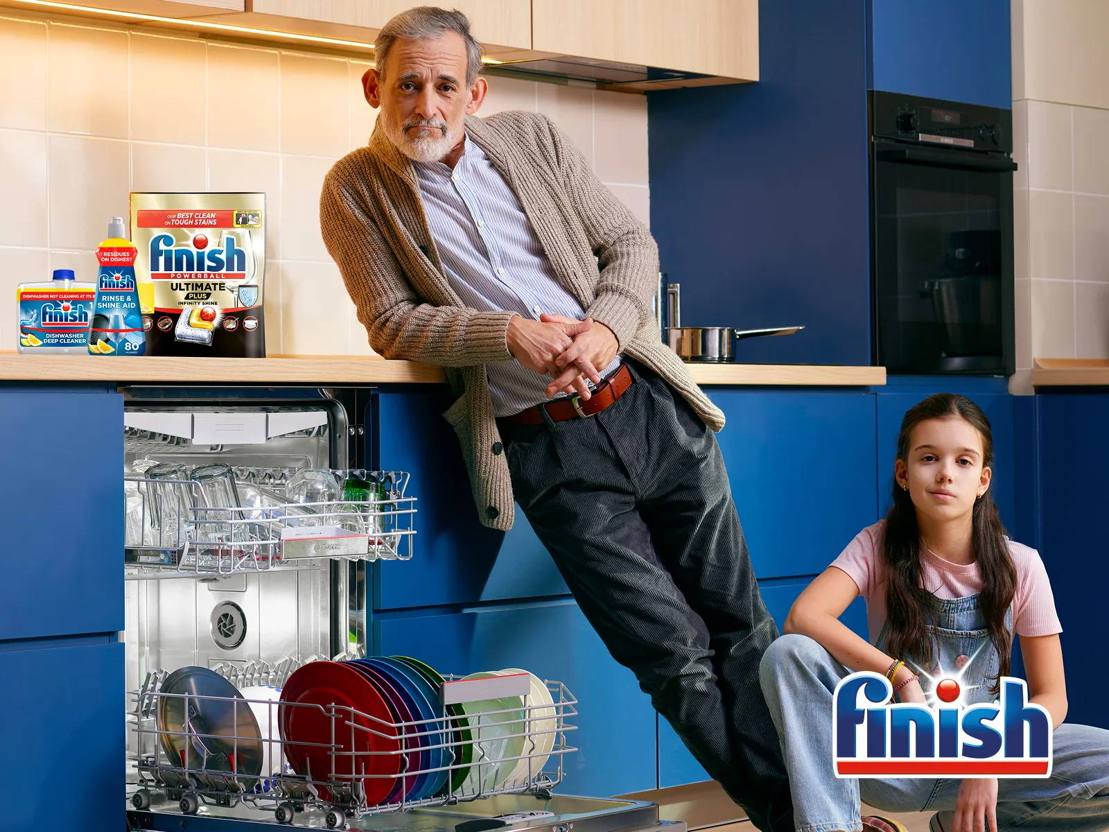 Adult and child in kitchen next to open Dishwasher with Finish pack on top