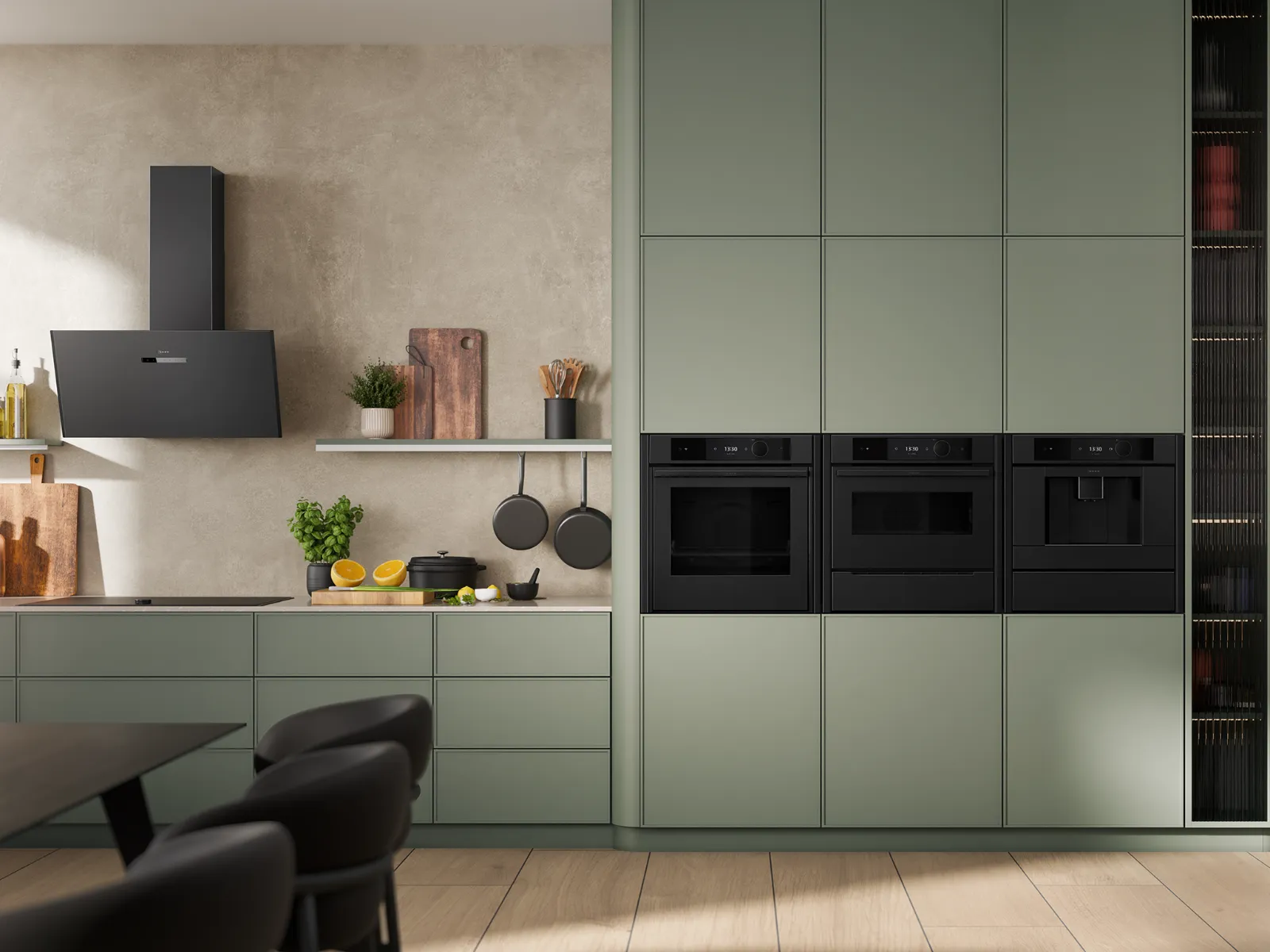 Modern kitchen interior with matte olive green cabinets, black built-in appliances, black chairs, and wooden floor and countertops.