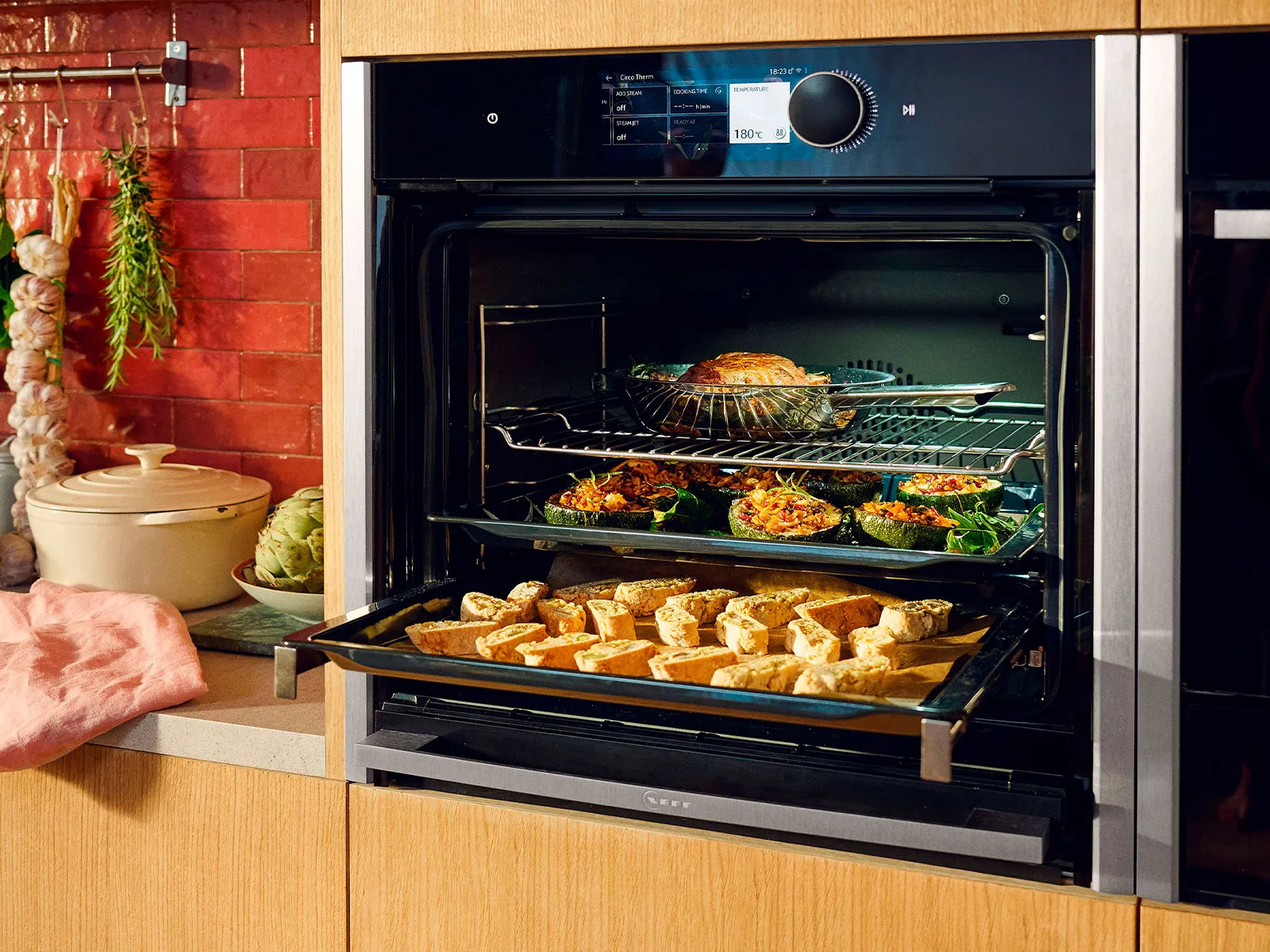 Cozy kitchen with baked goods in oven, cooking utensils, and herbs hanging on wall.