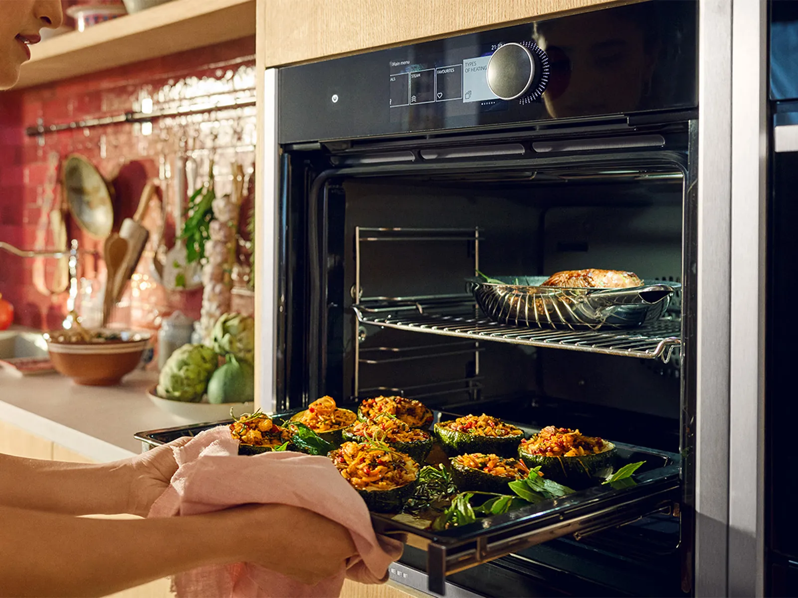 Person wearing oven mitts removing a tray of roasted vegetables from a kitchen oven.
