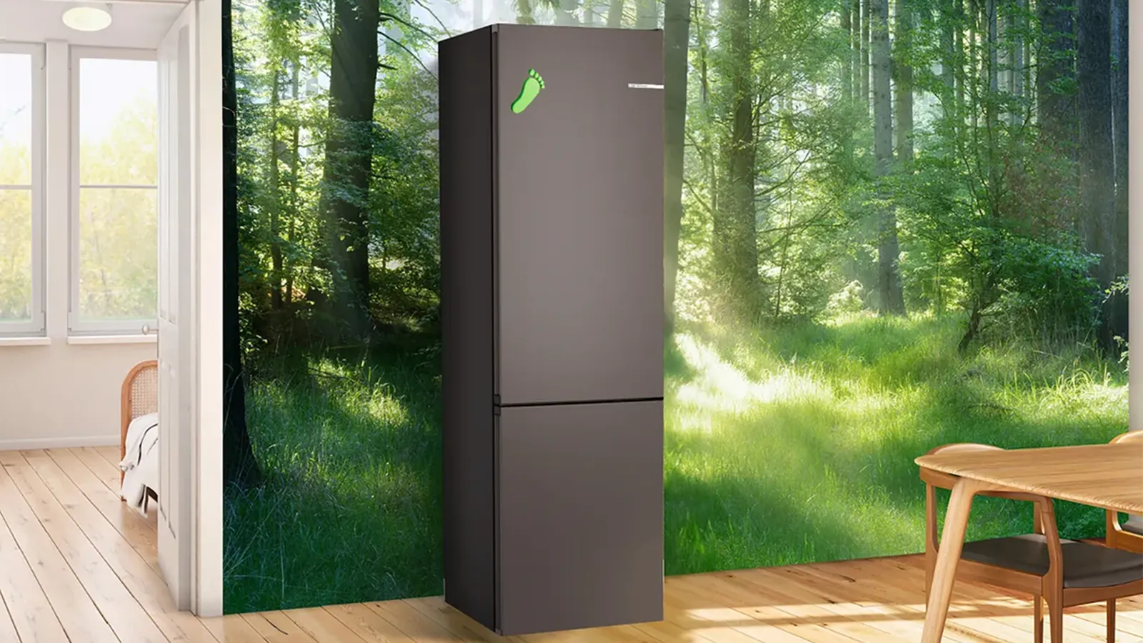 Freistehende, dunkelgraue Bosch Kühl-Gefrierkombination mit grünem Fußabdruck-Symbol vor einer Fototapete mit sonnigem Waldmotiv in einem hellen Wohnraum.
