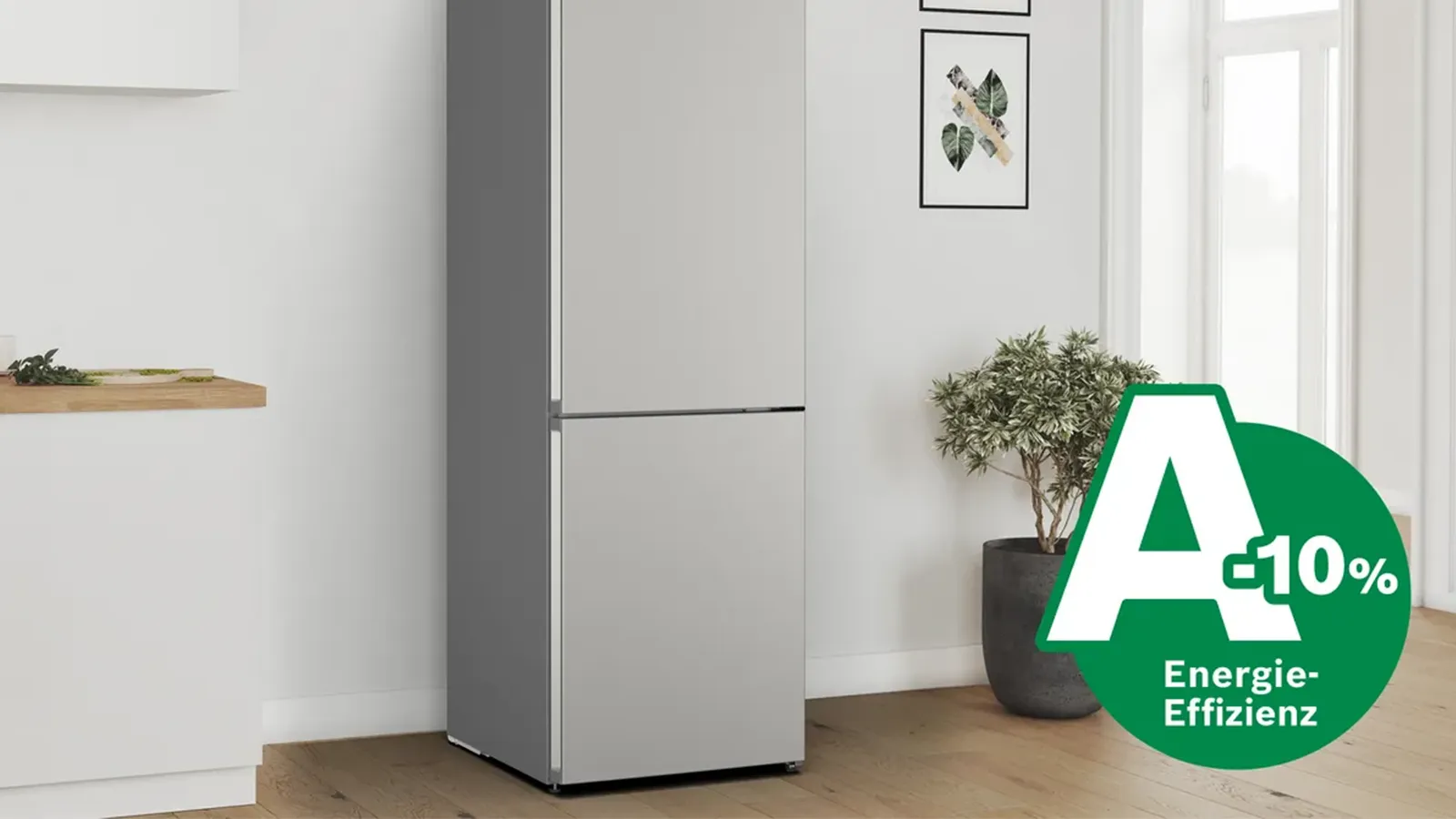 Freistehende, silberne Kühl-Gefrierkombination in einer hellen Küche mit einer eingeblendeten Grafik zur Energieeffizienzklasse „A -10%“.