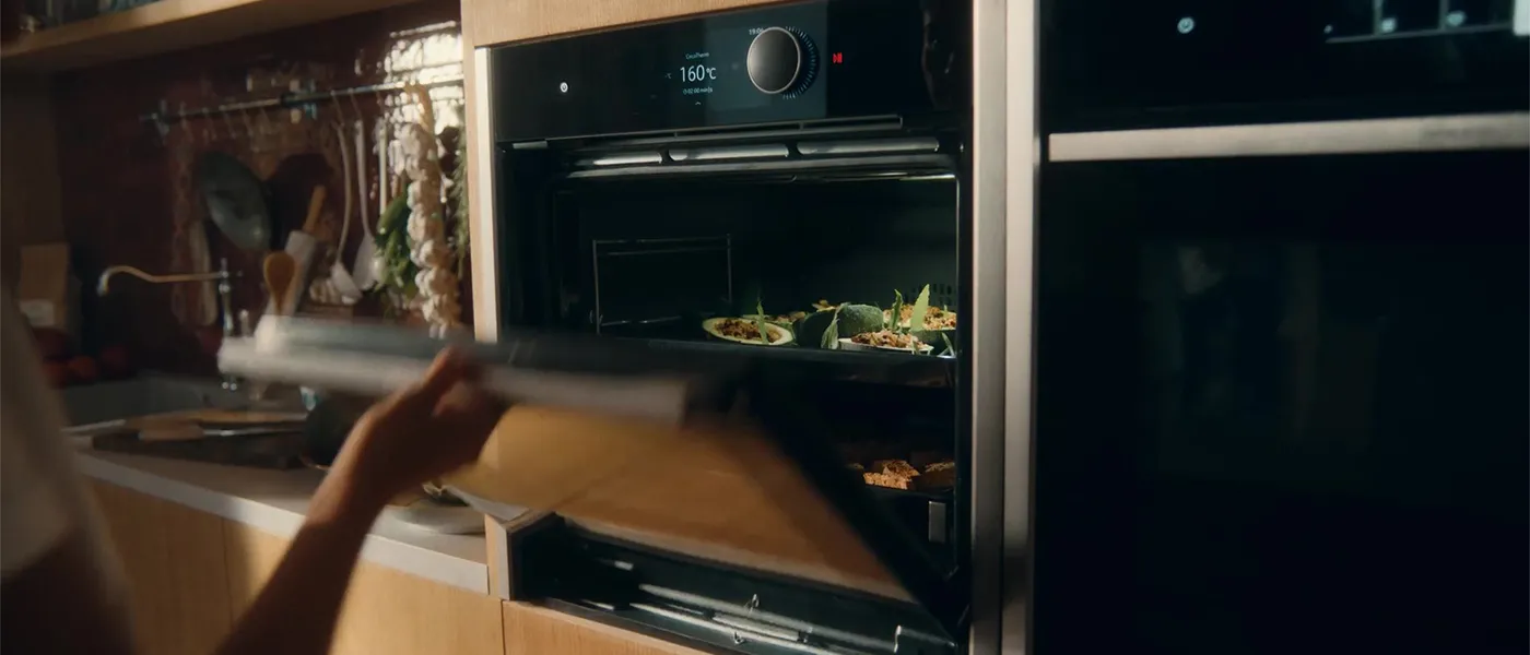 Forno con del cibo all'interno, porta aperta, mobili in legno e utensili da cucina in vista.