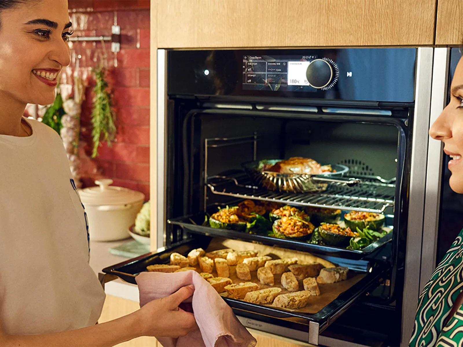 Two women preparing food together in a kitchen, with an open oven visible.
