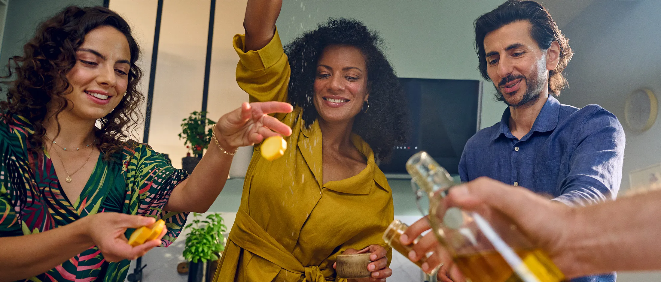 A group of friends laugh and enjoy cooking together in a modern kitchen, adding ingredients to their meal.