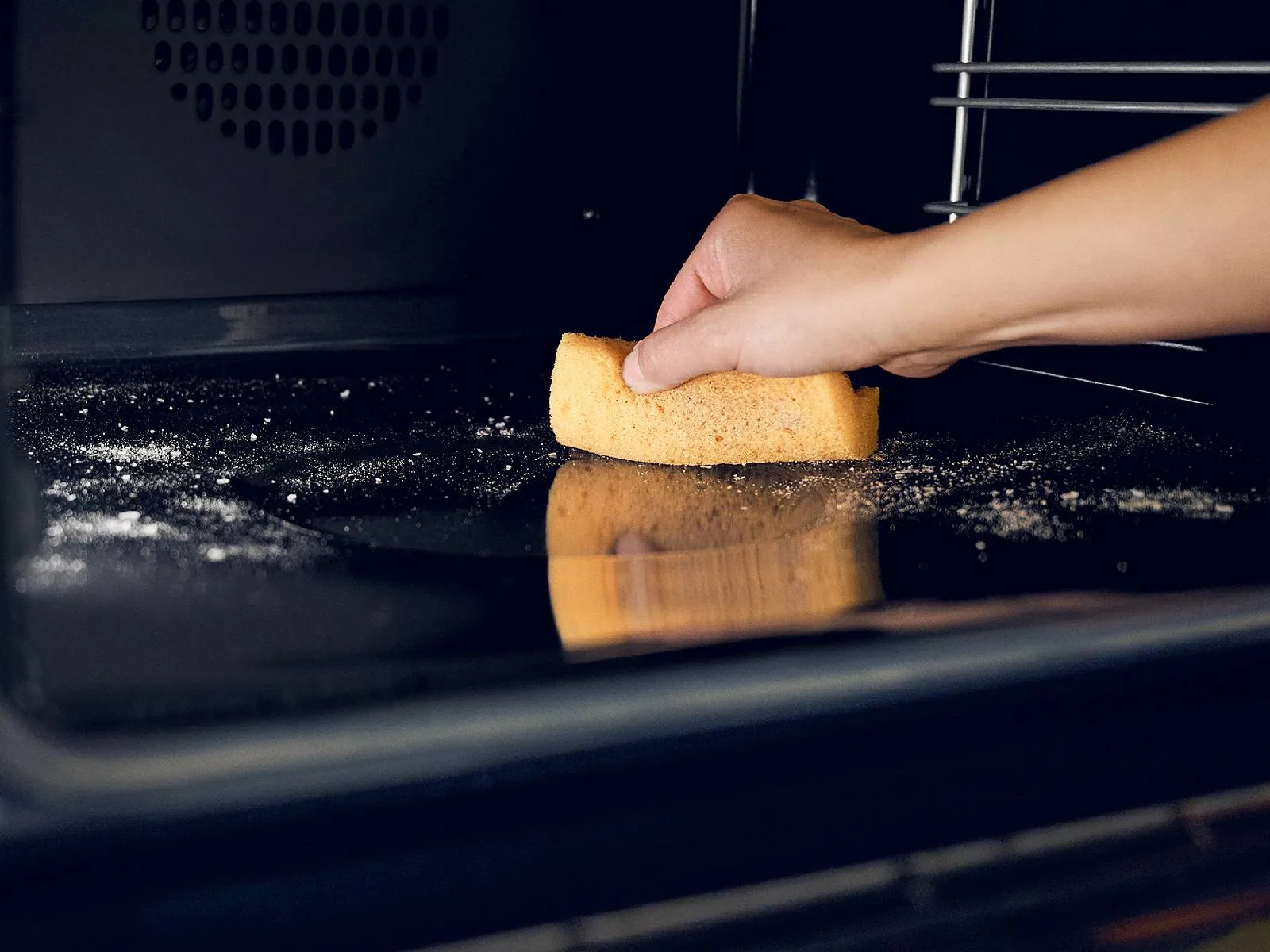 Hands placing a slice of bread in a dark oven, with flour visible on the surface.