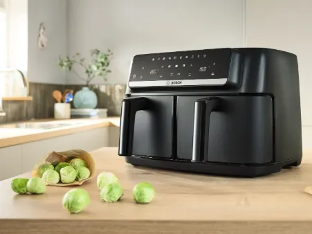 Black Bosch air fryer with digital display on a kitchen counter next to scattered Brussels sprouts and a brown paper bag.