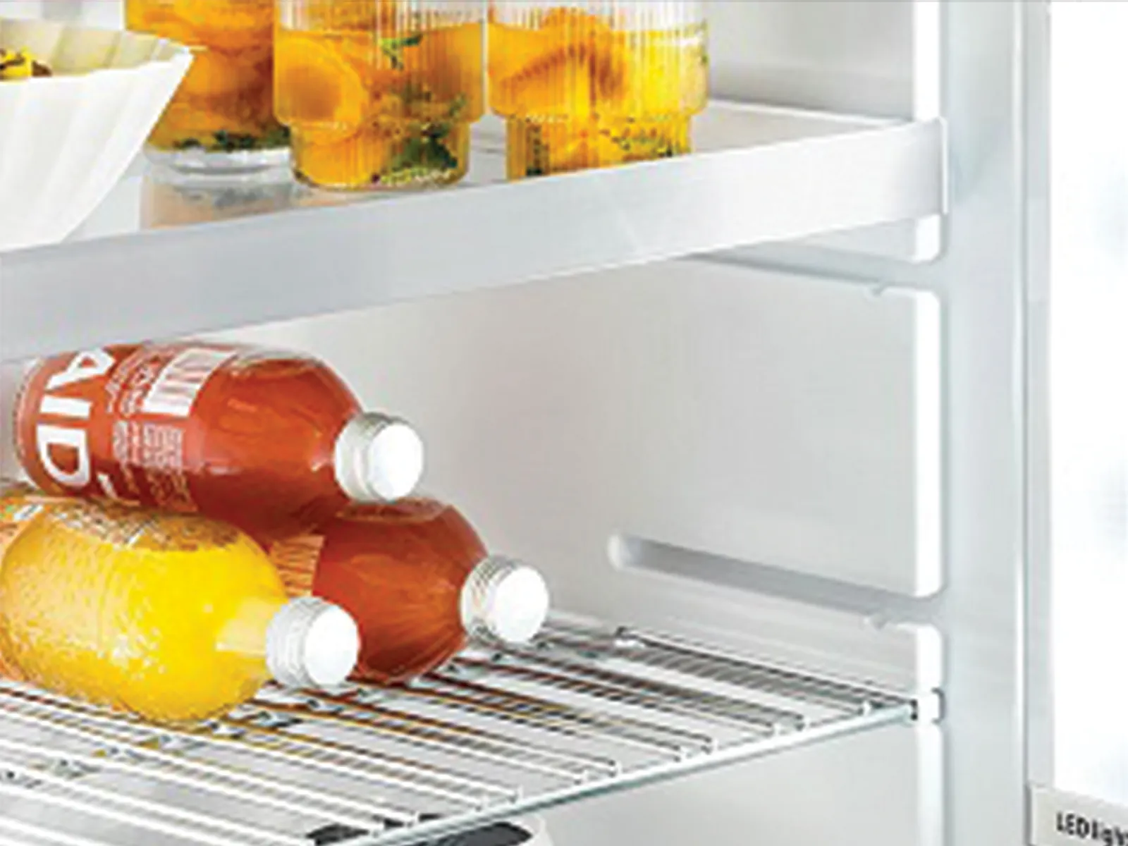 Eine geöffnete Kühlschranktür zeigt Ablagen voller Gläser mit fruchtiger Orangenmarmelade sowie Flaschen mit orangefarbenen und roten Getränken.