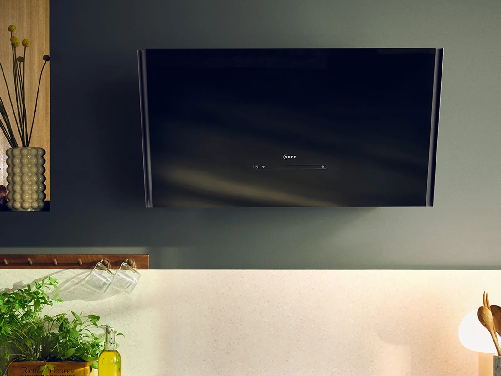 Wall-mounted TV, kitchen counter, plants, lamps, and decor items in a cozy, modern home interior.