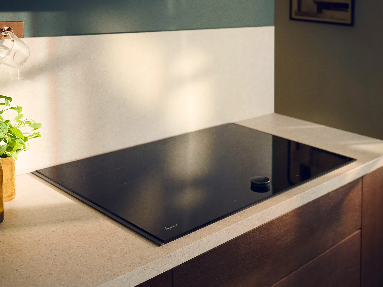 Black glass induction cooktop on a beige countertop in a modern kitchen with wooden cabinets and soft natural light.