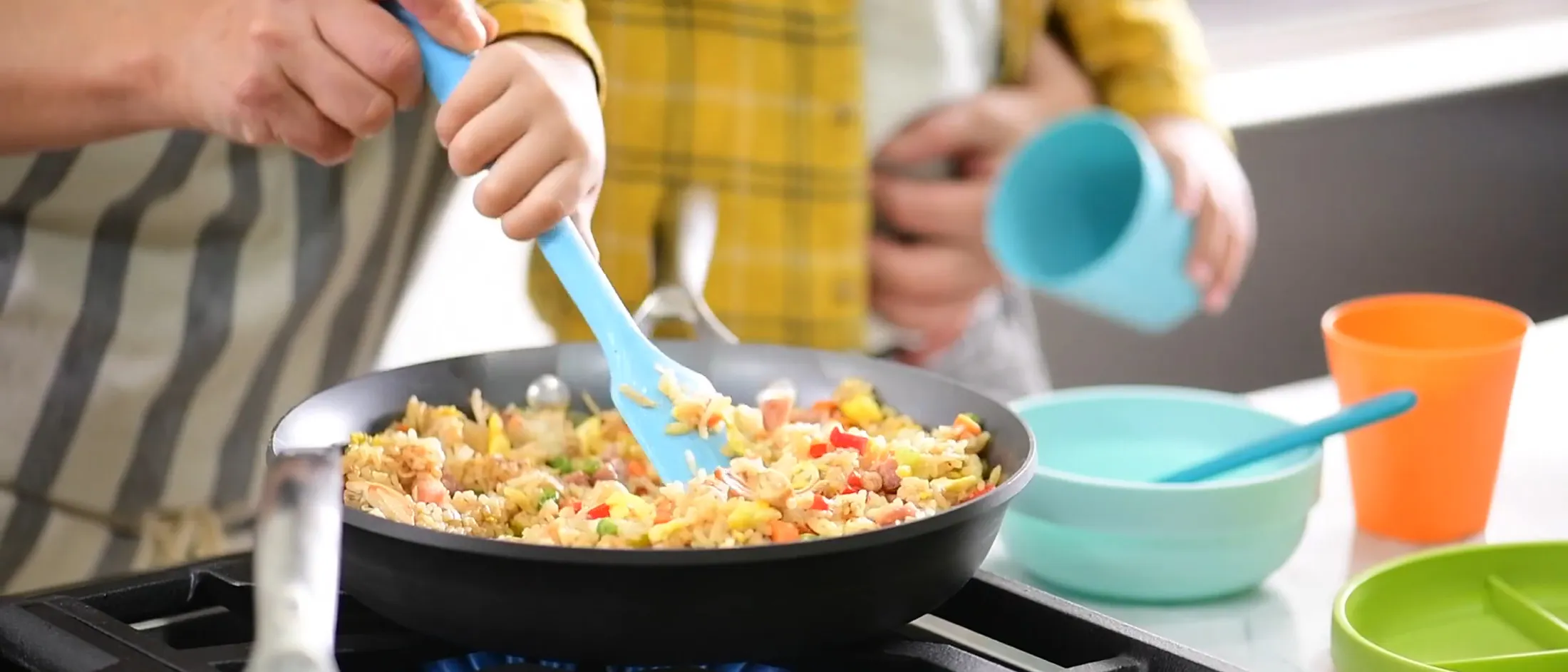 Pan frying a colorful mix of rice, eggs, vegetables, and ham in a skillet with a blue spatula on a stovetop.