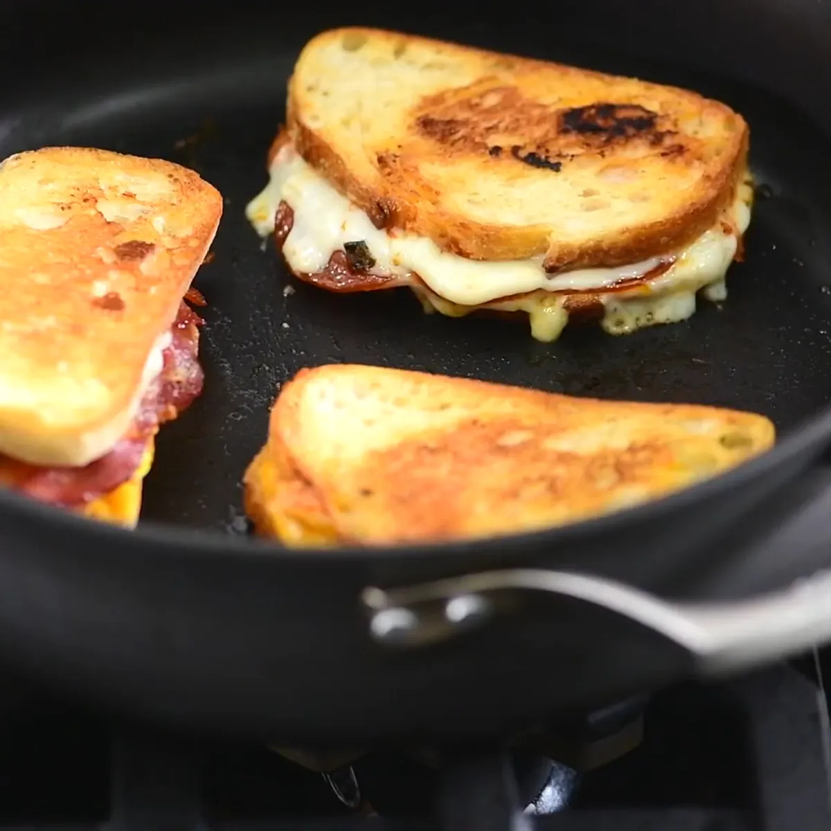 Person assembling sandwiches with various ingredients like cheese, lettuce, tomato, and bacon on a wooden cutting board.