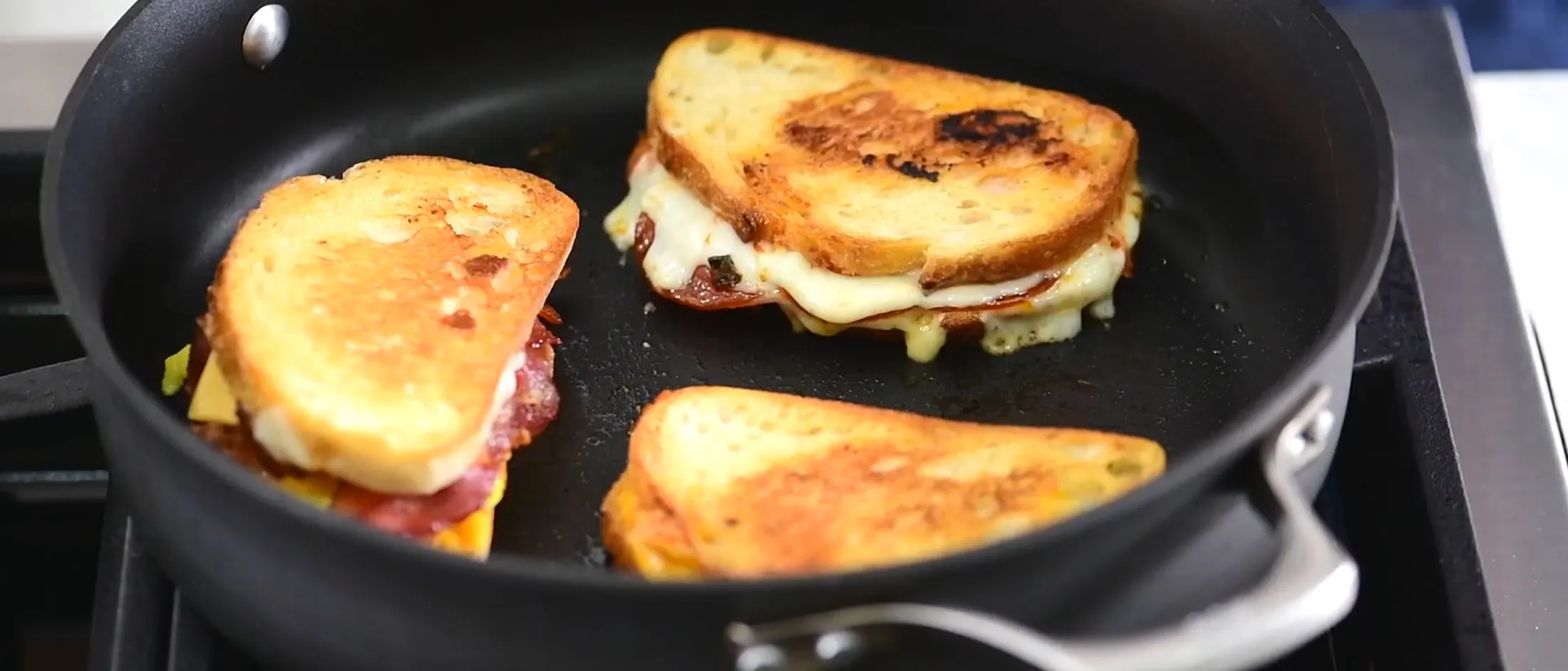 Person assembling sandwiches with various ingredients like cheese, lettuce, tomato, and bacon on a wooden cutting board.