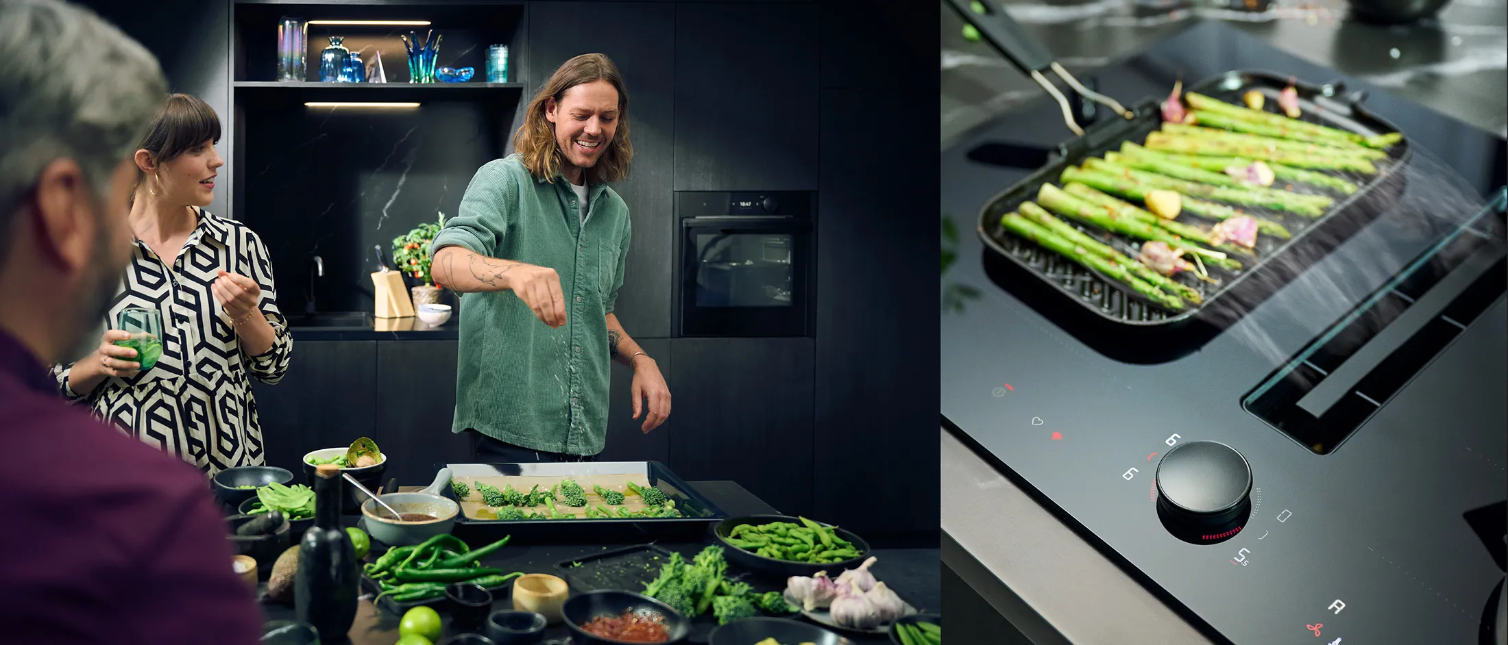 Man cooking asparagus on a grill pan while two people watch and chat in a modern kitchen.