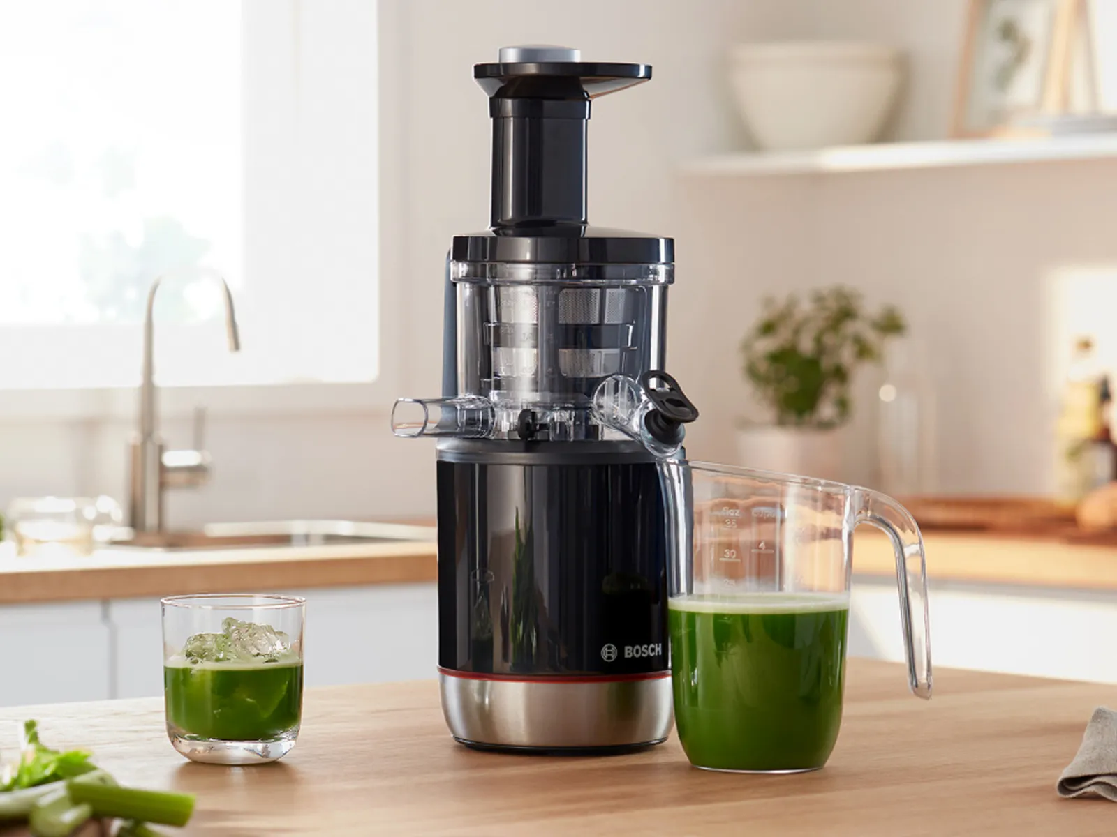 Шнековая соковыжималка Bosch VitaJuice с зеленым соком стоит на кухонной столешнице.