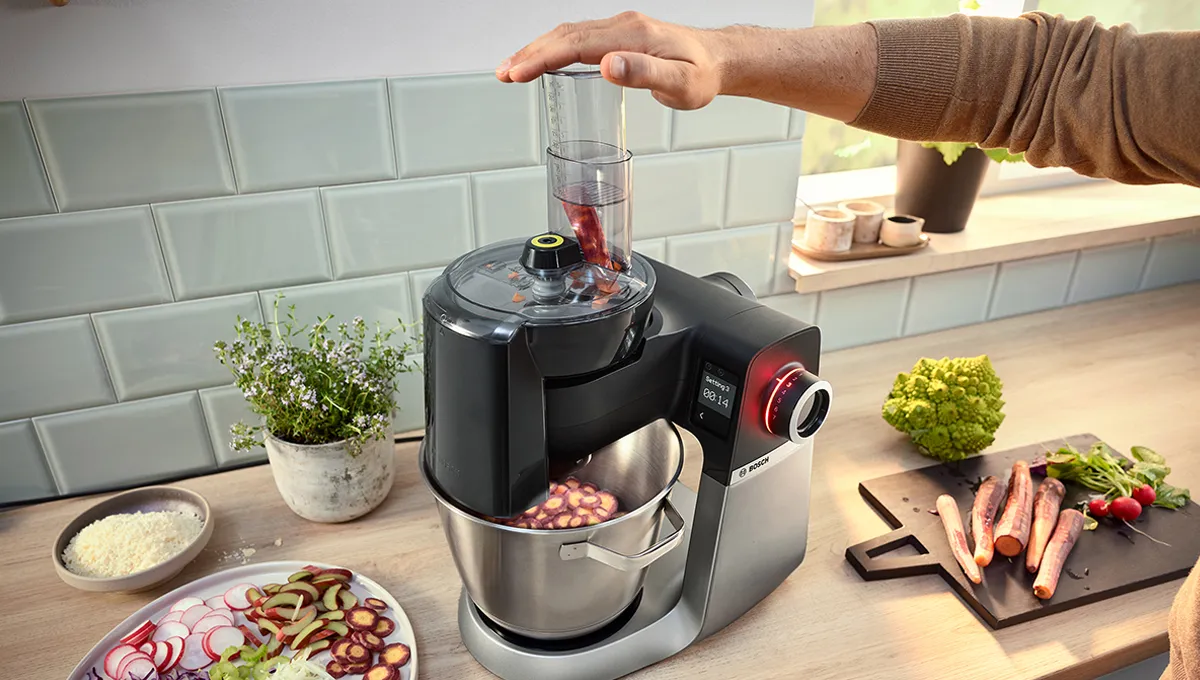 Series 6 stand mikseri rəndə diskləri ilə tərəvəzləri emal edir; yanında hazır dilimlənmiş salat tərəvəzləri və kök ilə turplardan ibarət kəsmə lövhəsi.