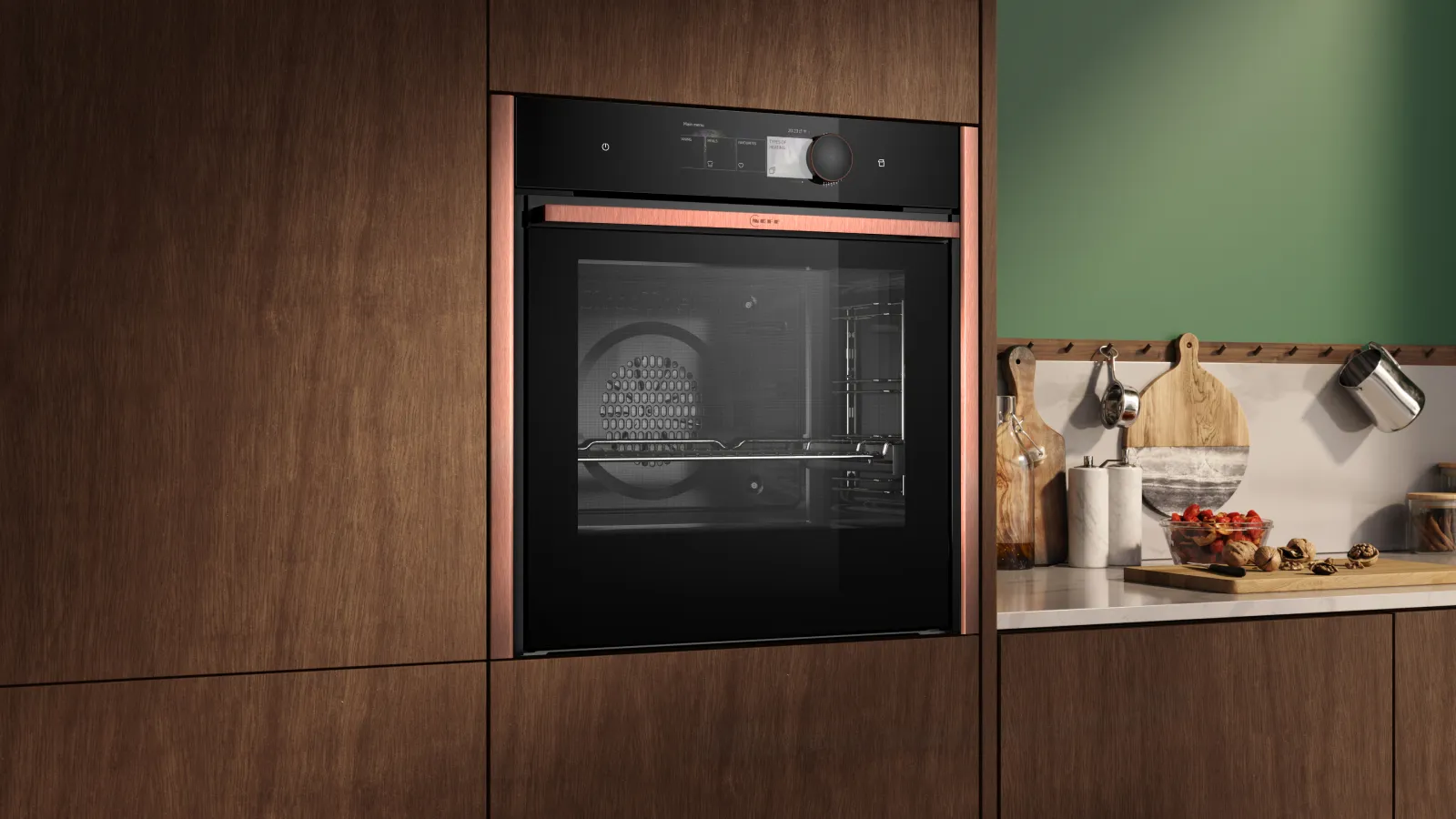 NEFF B69VY7MY0 oven in Flex Design Brushed Bronze in wood cabinets beside a countertop with cutting boards, jars and a bowl of fruit.